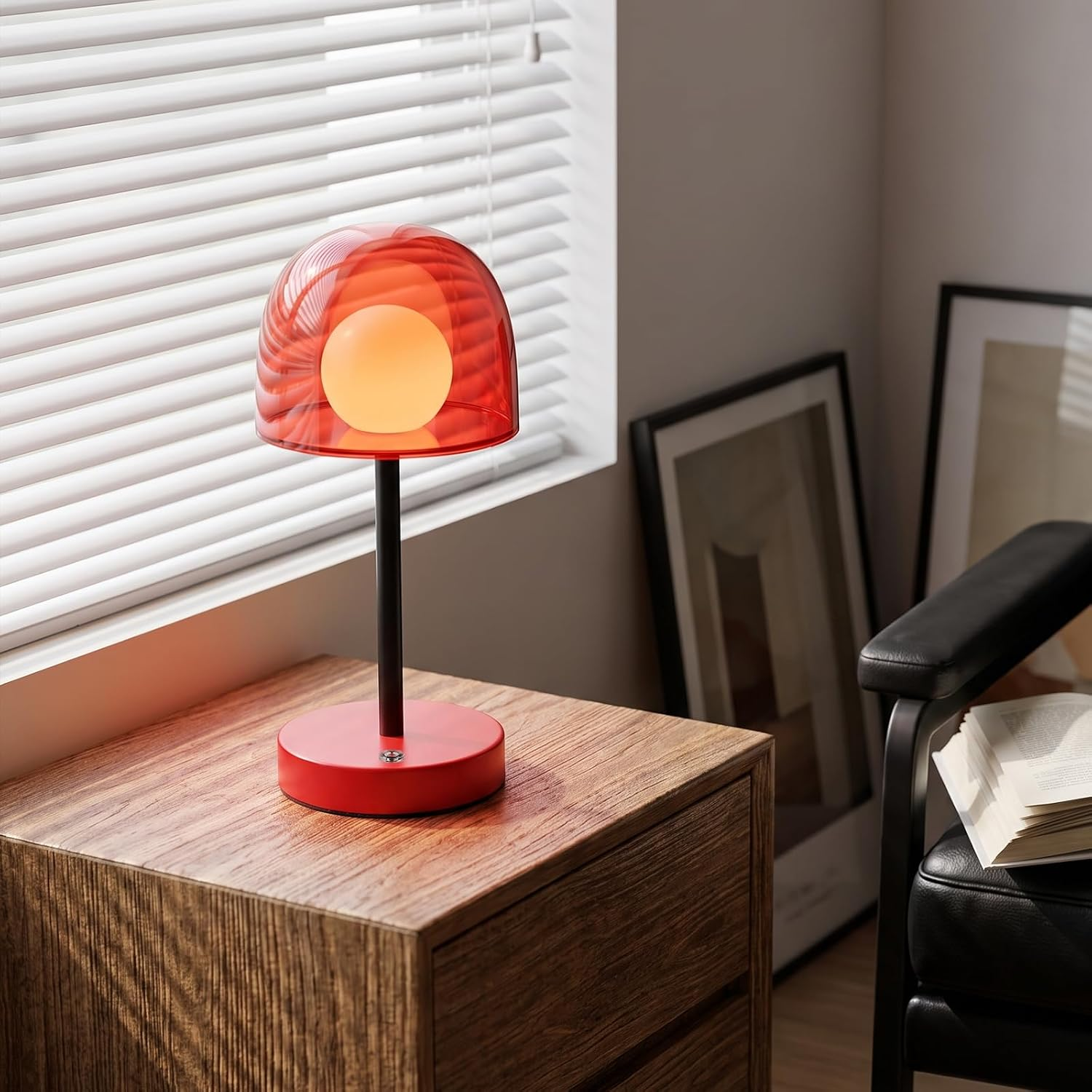 Eine rote Tischlampe auf einem Holztisch vor einer Jalousie, neben einem Stuhl.