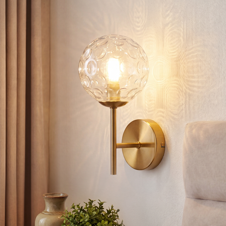 Eine goldene Wandlampe mit strukturierter Glaskugel strahlt warmes Licht an eine helle Wand.