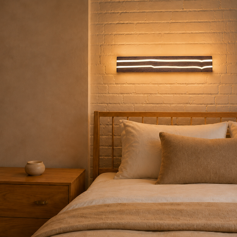 Ein hölzernes Bett mit weißen Kissen steht an einer weißen Backsteinwand mit einer beleuchteten Holzwandleuchte.