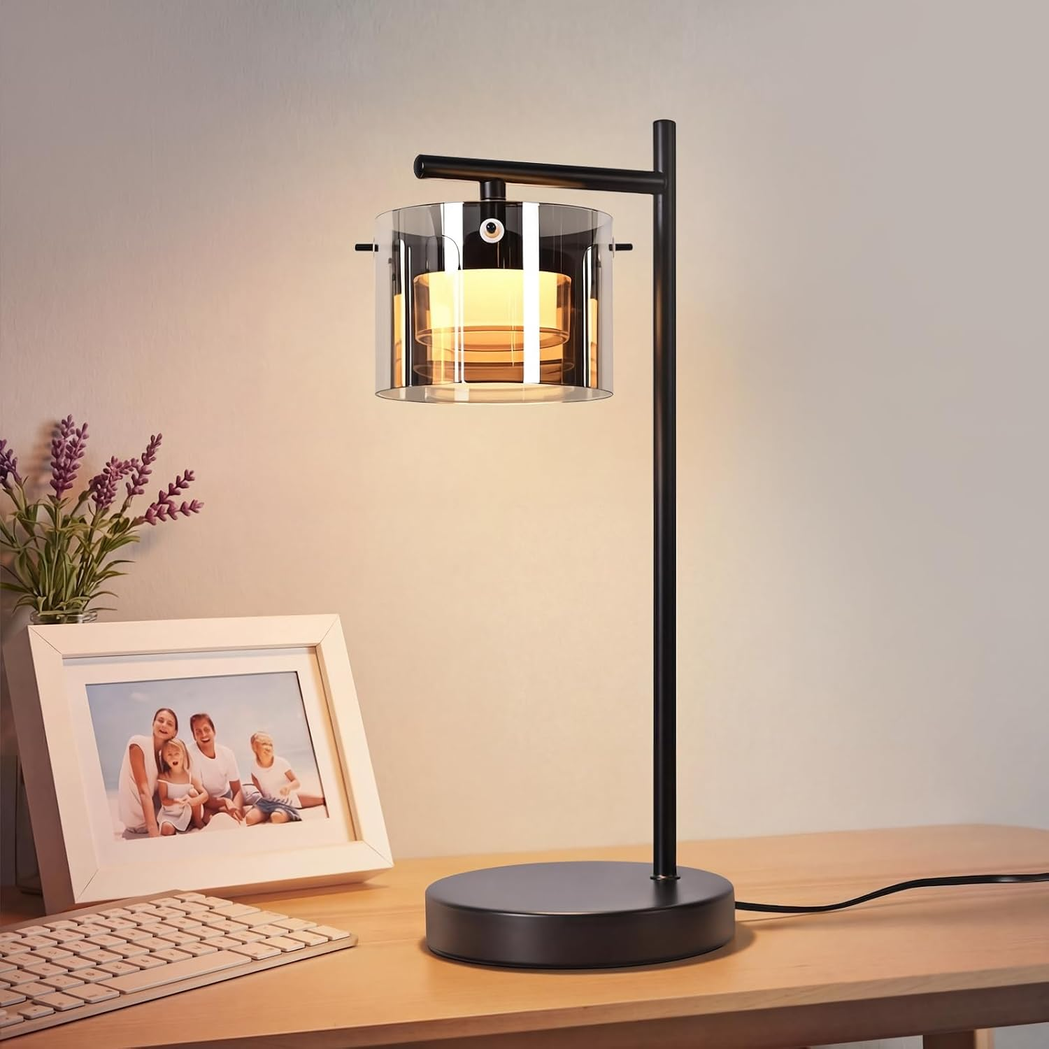 Moderne schwarze Schreibtischlampe mit Glas- und Warmlichtschirm neben einem Familienfoto und einer Tastatur auf Holz.