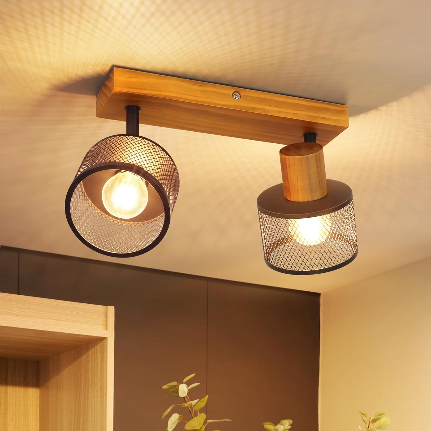 Eine Deckenlampe mit Holzsockel und zwei schwarz-gitterartigen Strahlern leuchtet warm an der Decke.