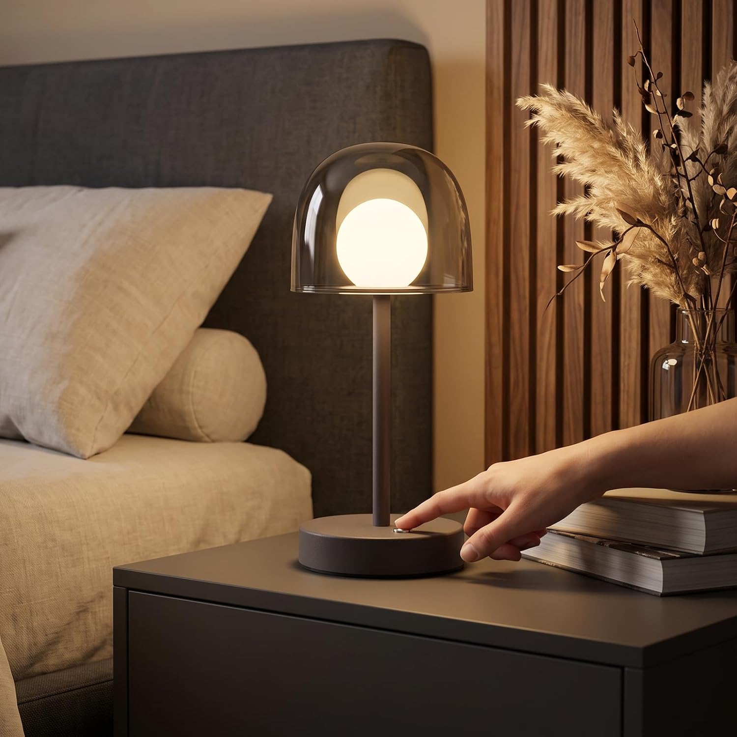 Eine Hand schaltet eine moderne Tischlampe mit leuchtender Kugel auf einem Nachttisch ein.