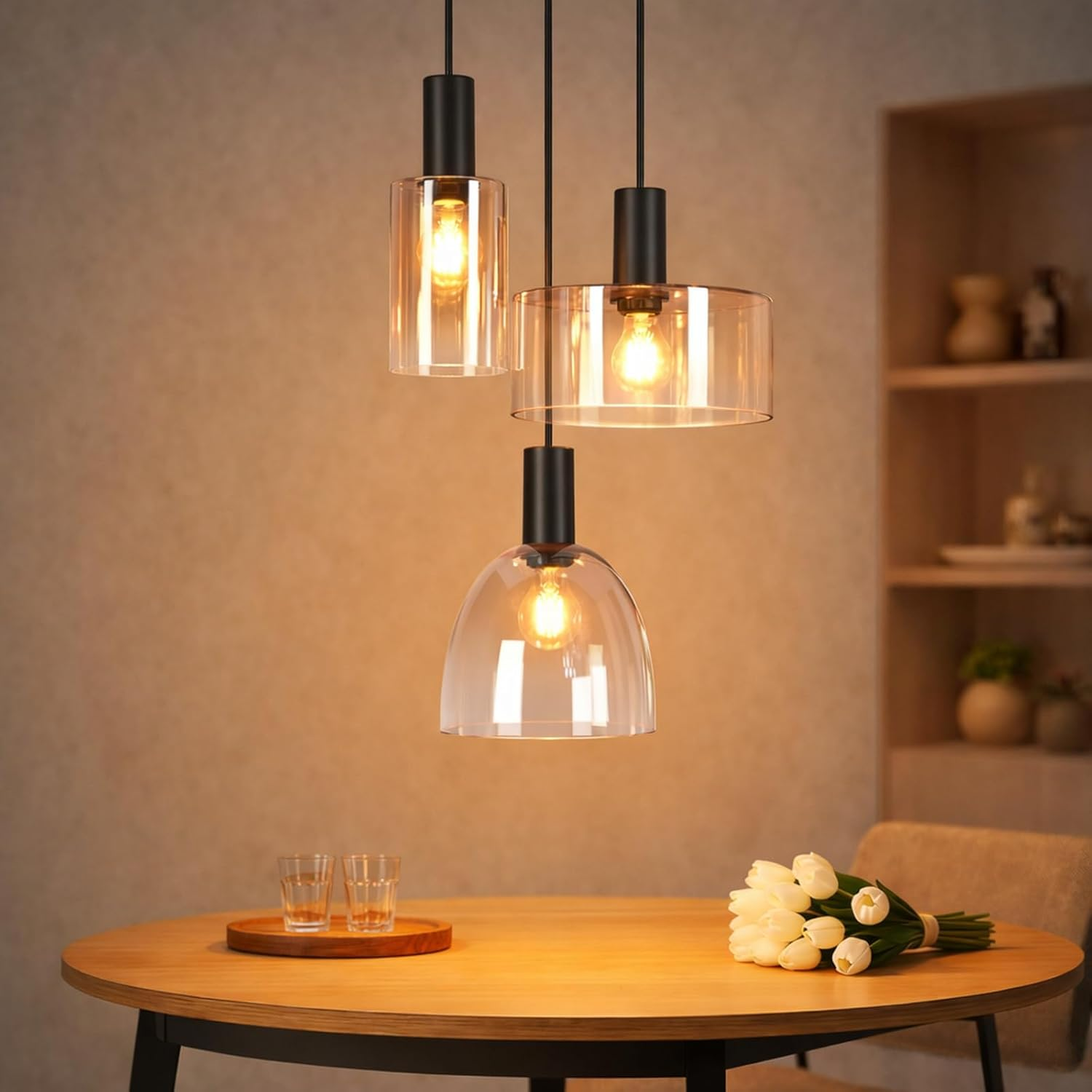 Drei moderne Hängelampen mit Glasschirmen leuchten über einem Holztisch mit Blumen und Gläsern.