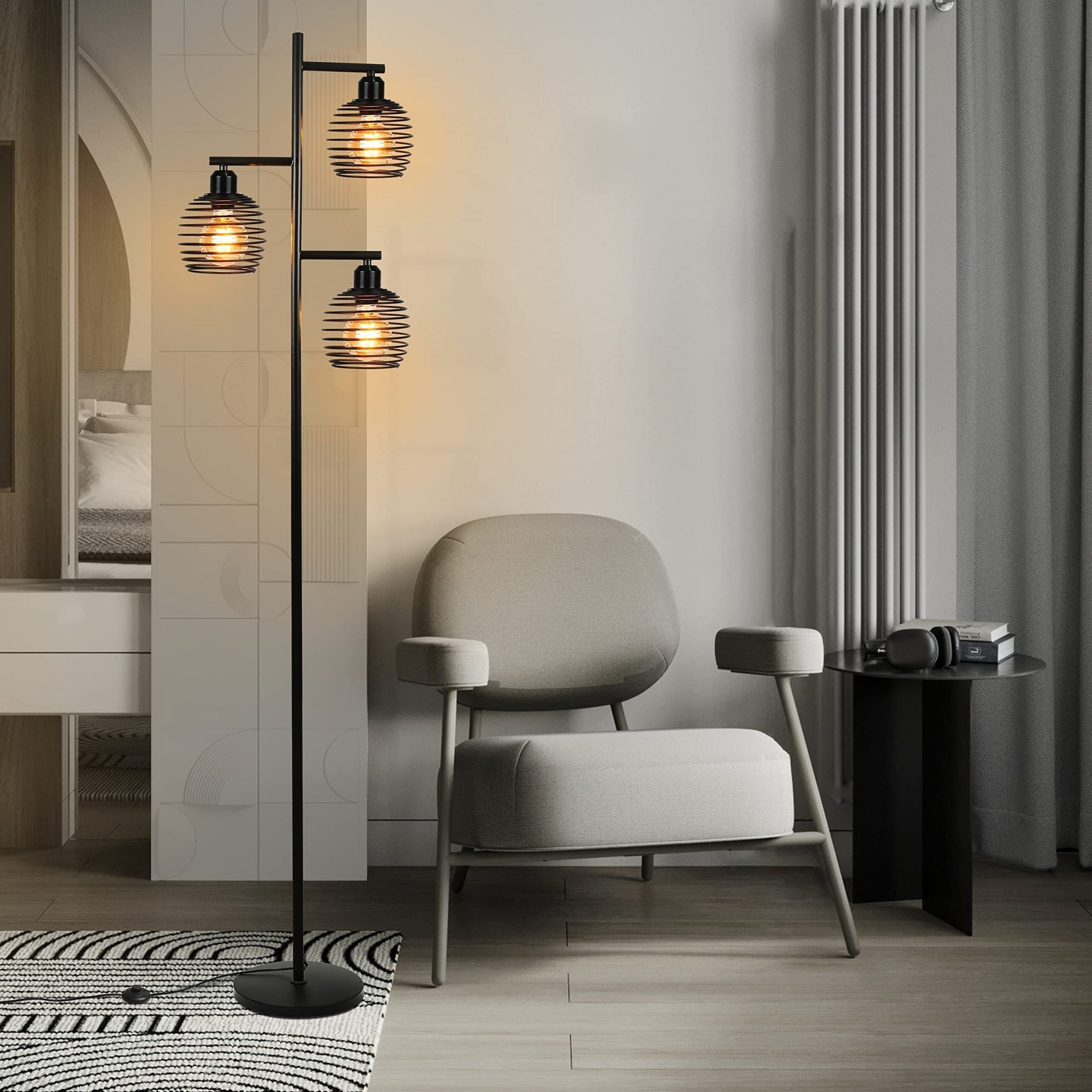 Eine schwarze Stehlampe mit drei Glühbirnen neben einem grauen Sessel in einem modernen Raum.