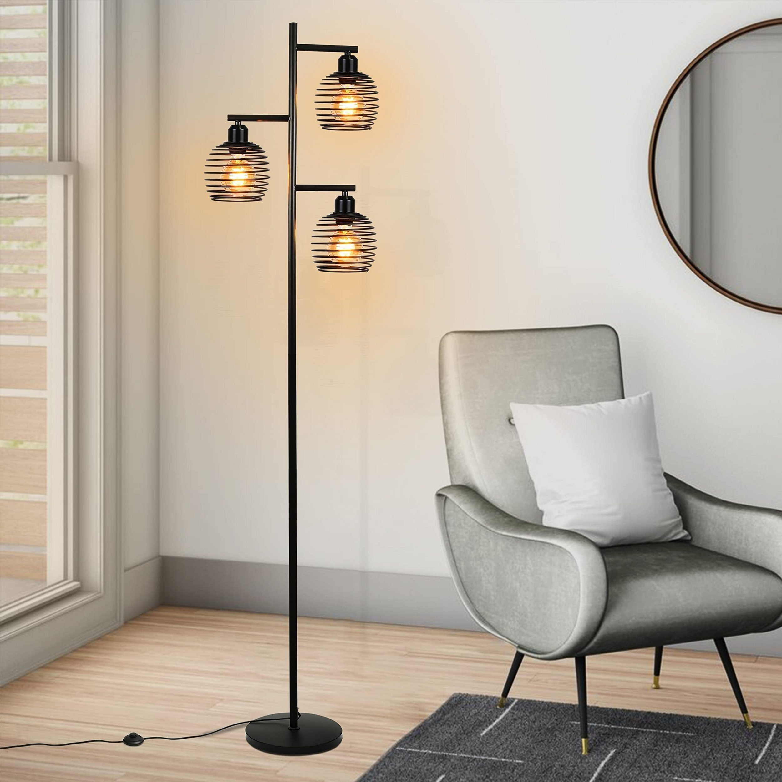 Eine schwarze Stehlampe mit drei Glühbirnen steht in einem modernen Wohnzimmer neben einem grauen Sessel.