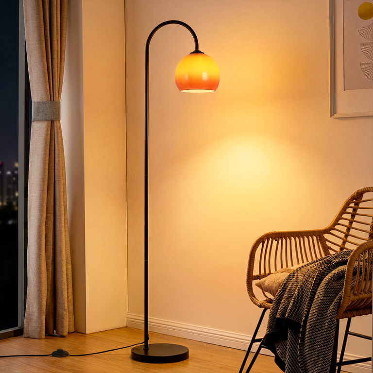 Eine schwarze Bogenlampe mit orangefarbenem Glasschirm steht in einem gemütlichen Raum neben einem Rattansessel.