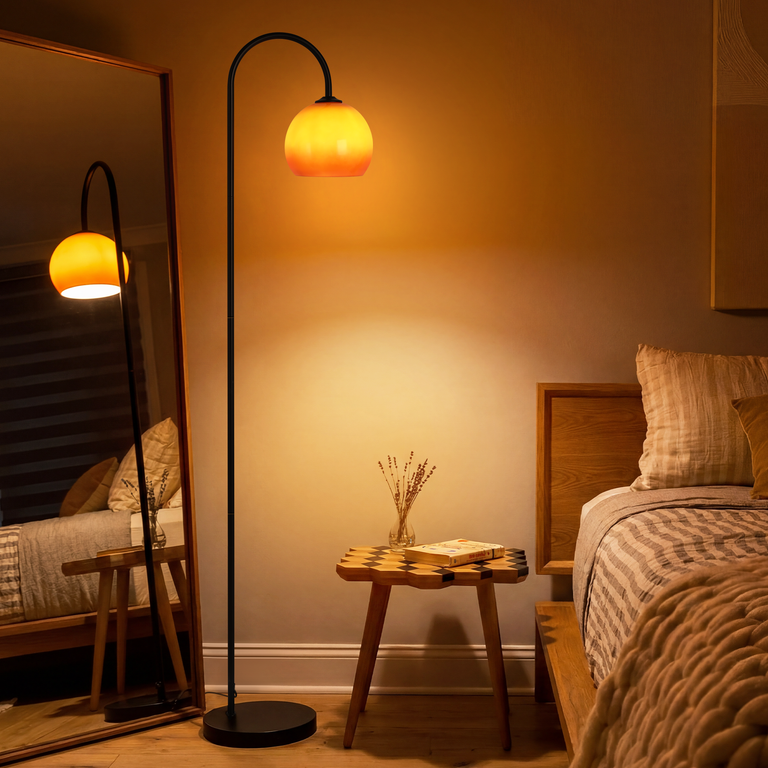 Eine schwarze Bogenlampe mit orangefarbenem Schirm steht im Schlafzimmer neben einem Nachttisch mit Buch.