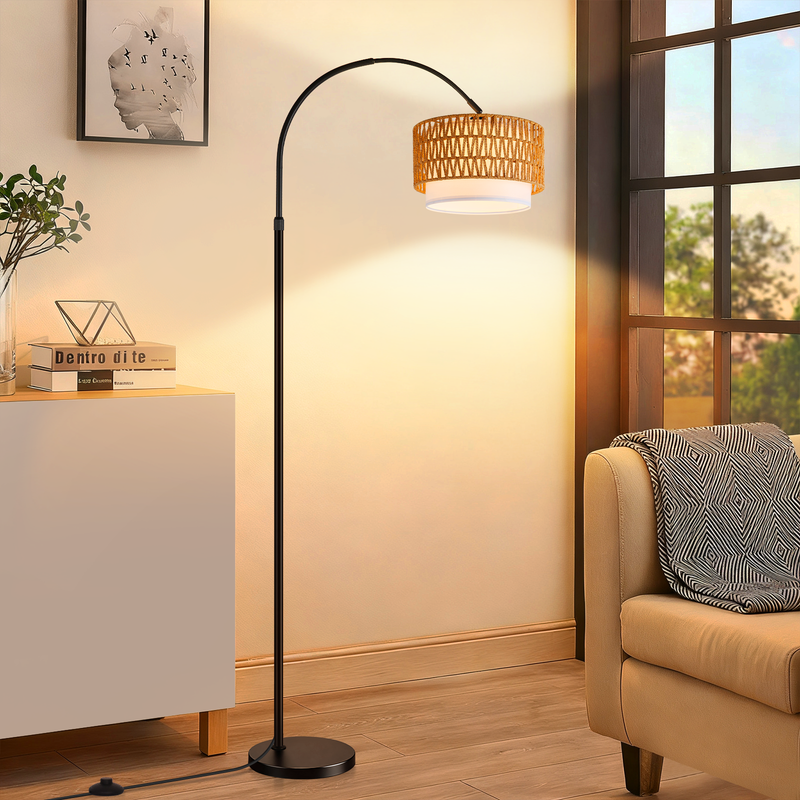 Eine schwarze Bogenstehlampe mit geflochtenem Lampenschirm steht neben einem Sofa in einem hellen Wohnzimmer.