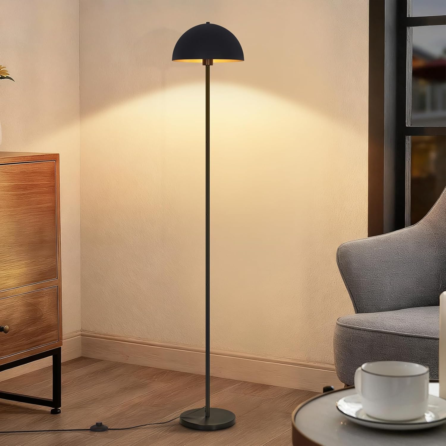 Eine schwarze Stehlampe mit halbkugelförmigem Schirm strahlt warmes Licht an eine helle Wand in einem gemütlichen Raum.