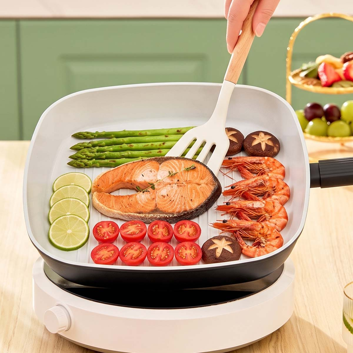 Una mano usa una espátula para voltear salmón, camarones, espárragos, tomates, limas y champiñones en una sartén cuadrada.