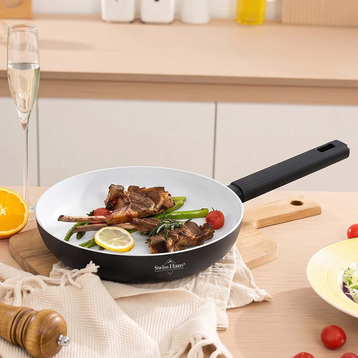 Eine schwarze Bratpfanne mit gebratenen Lammkoteletts, Zitronenscheiben und Spargel auf einem Holztisch.