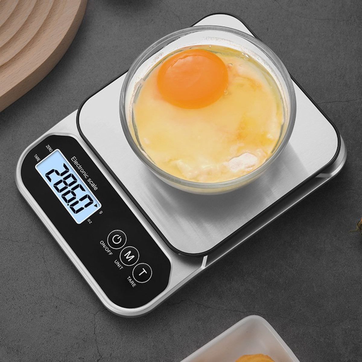 Eine digitale Küchenwaage mit einer Glas Schüssel, die ein rohes Ei enthält, auf einer dunklen Arbeitsplatte.