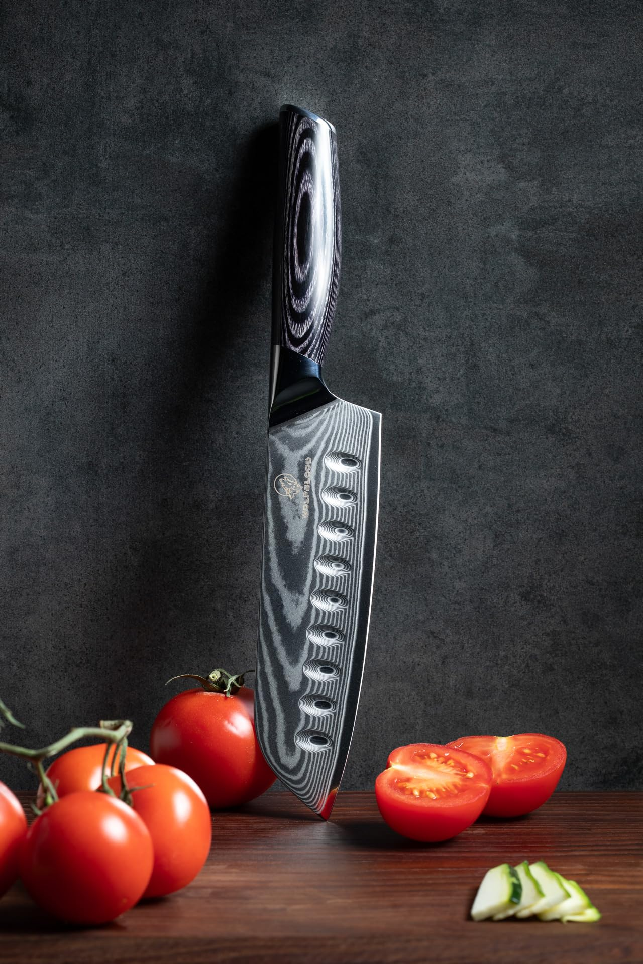 Un couteau de Damas posé verticalement sur du bois avec des tomates rouges et des tranches de concombre.
