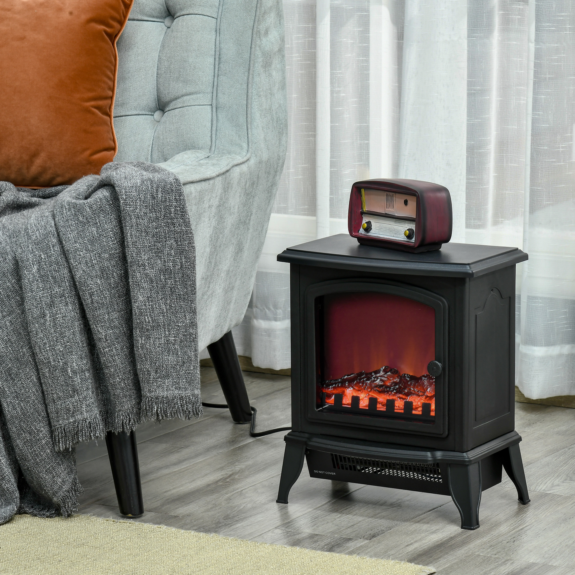 Un pequeño calefactor eléctrico de chimenea con ascuas brillantes junto a un sillón gris con una manta.