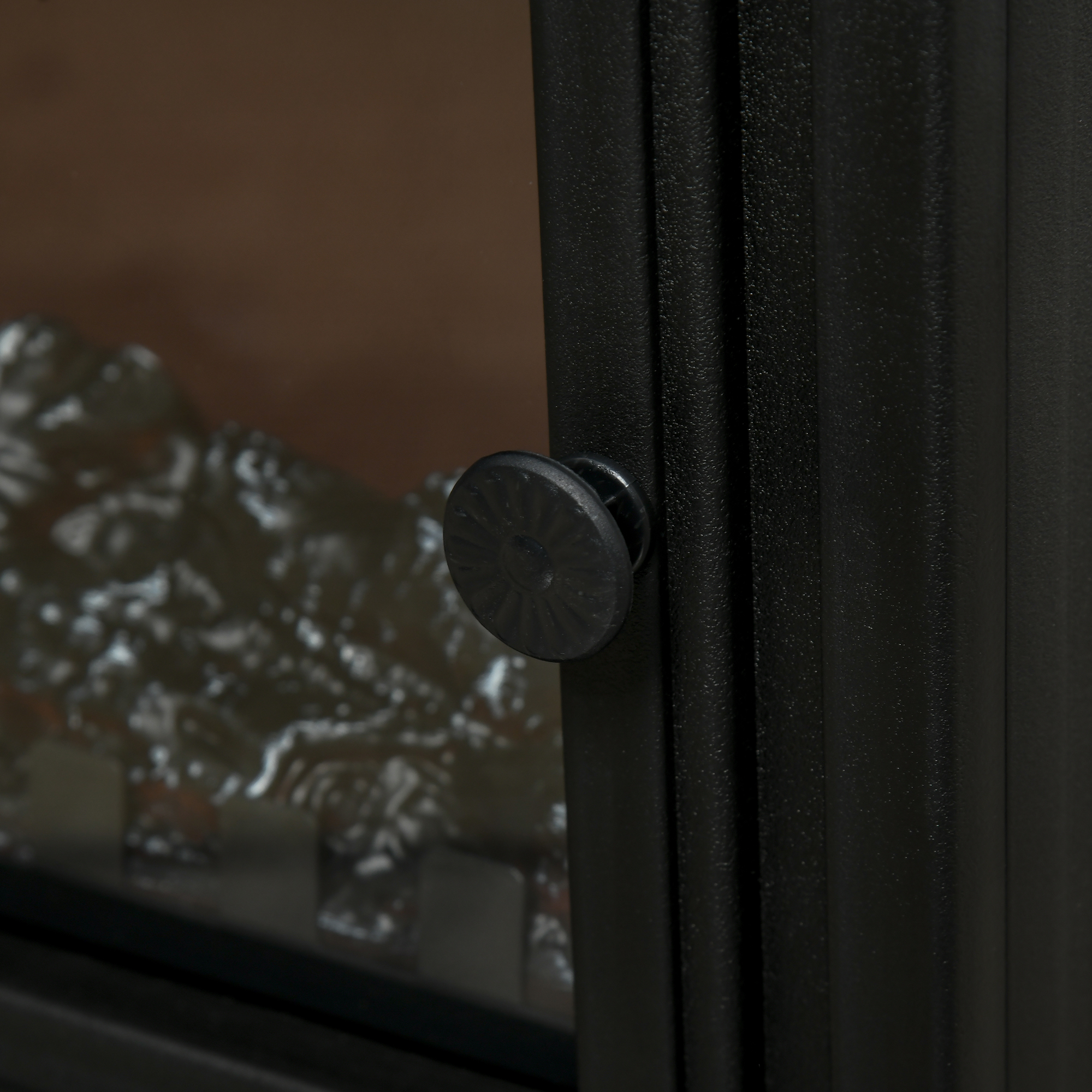 Primer plano de un pomo de armario negro en una puerta metálica con piezas de brasa artificiales al fondo.