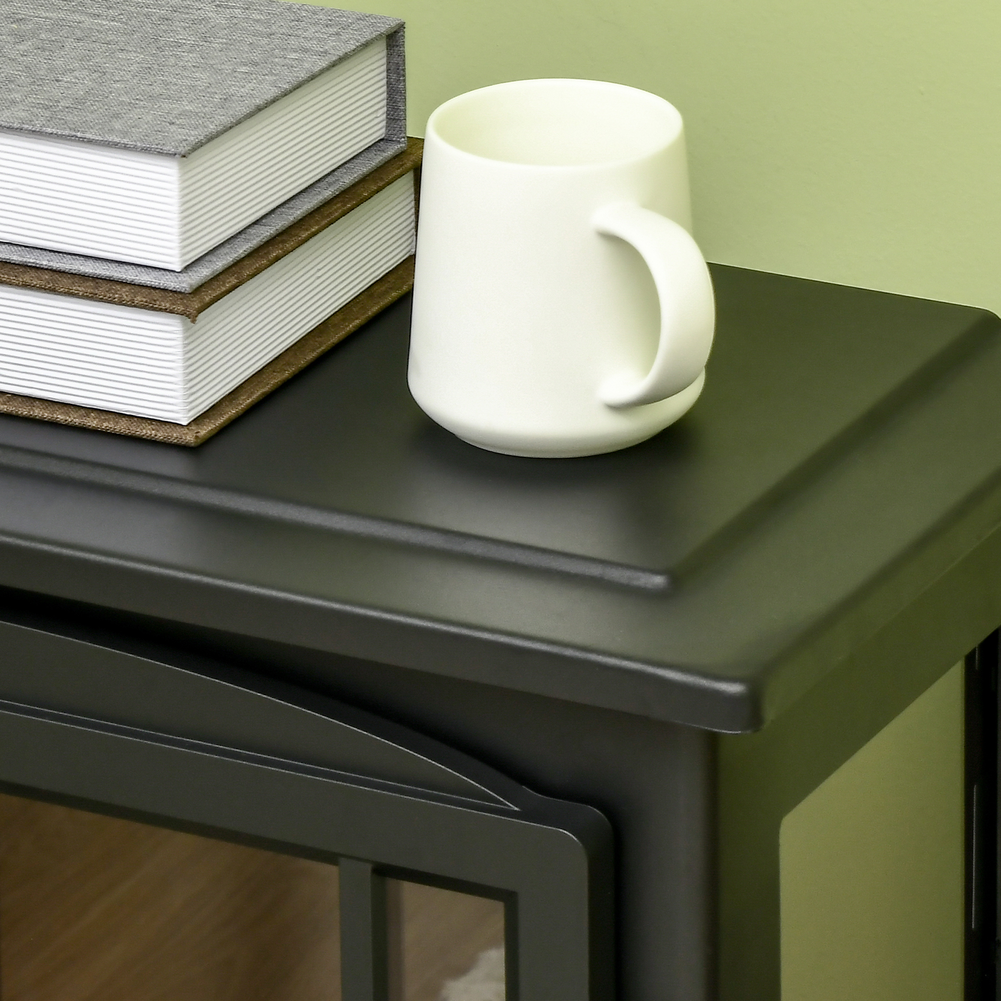 Una taza blanca y dos libros están sobre una mesa negra contra una pared verde.