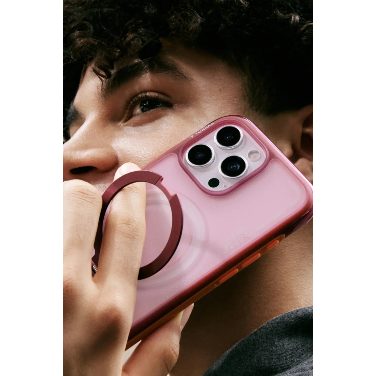 Bir adam yüzünün yanında halka standlı pembe bir akıllı telefon tutuyor.
