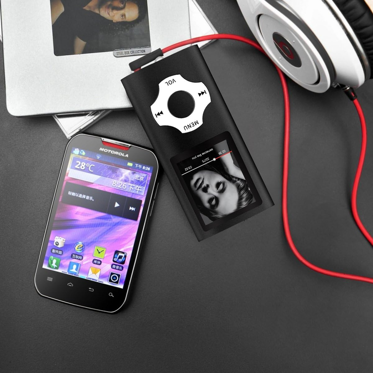 Ein Smartphone, ein MP3-Player mit Kopfhörern und ein Notebook liegen auf einer dunklen Oberfläche.