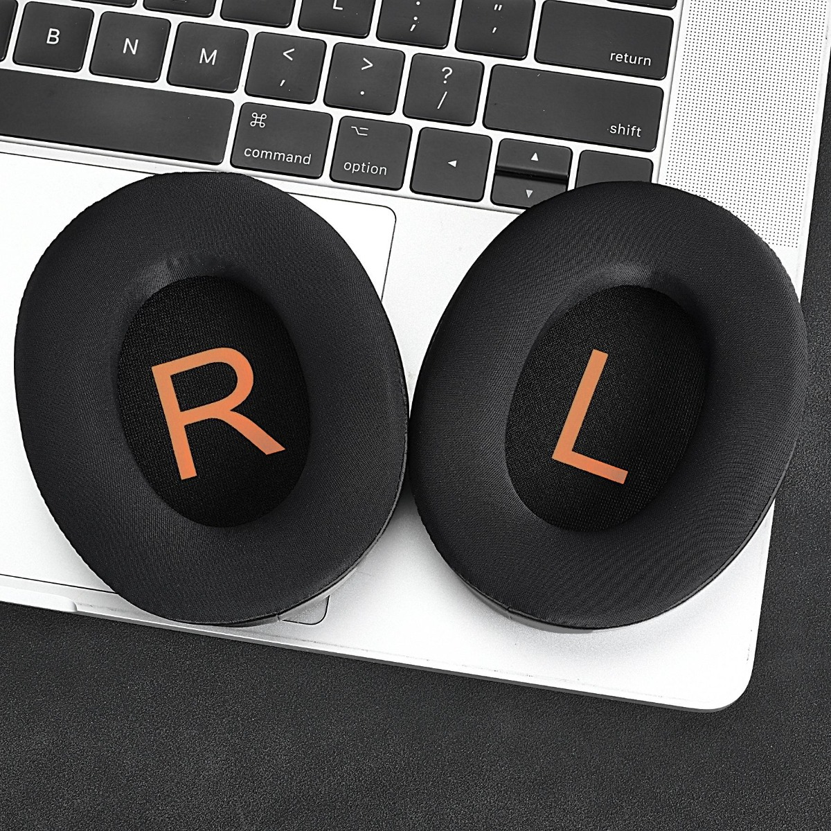 Zwei schwarze Ohrpolster mit orangefarbenem R und L liegen auf einem Laptop.