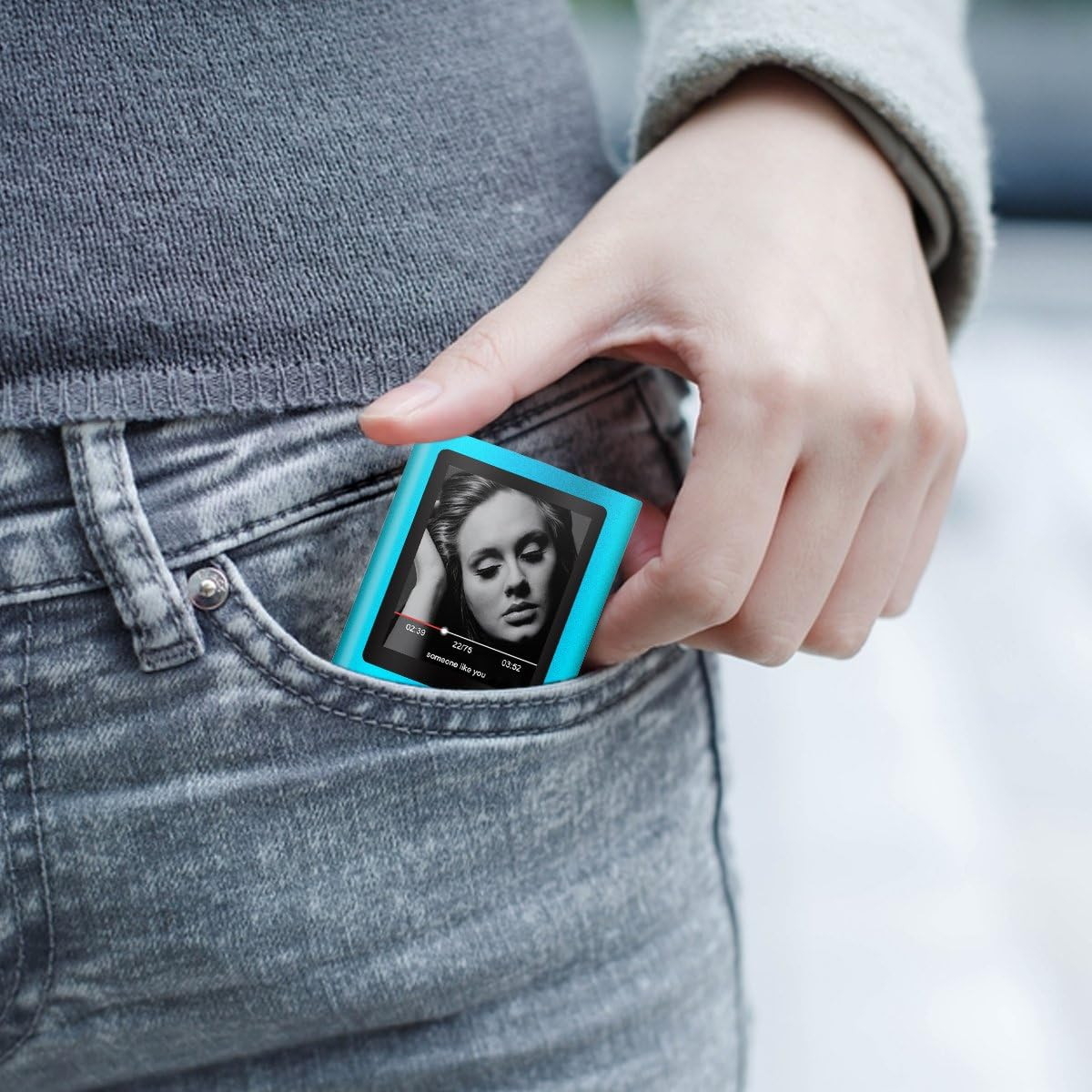 Eine Hand steckt einen hellblauen Musikplayer in eine graue Jeanshosentasche.