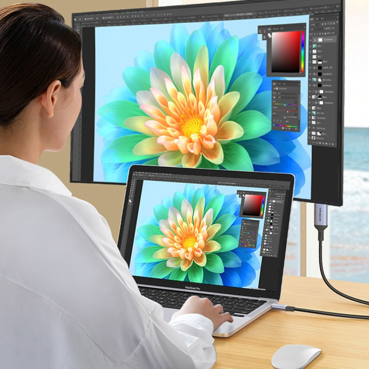 Eine Frau bearbeitet das Foto einer bunten Blume auf ihrem Laptop, angezeigt auf einem großen Monitor.