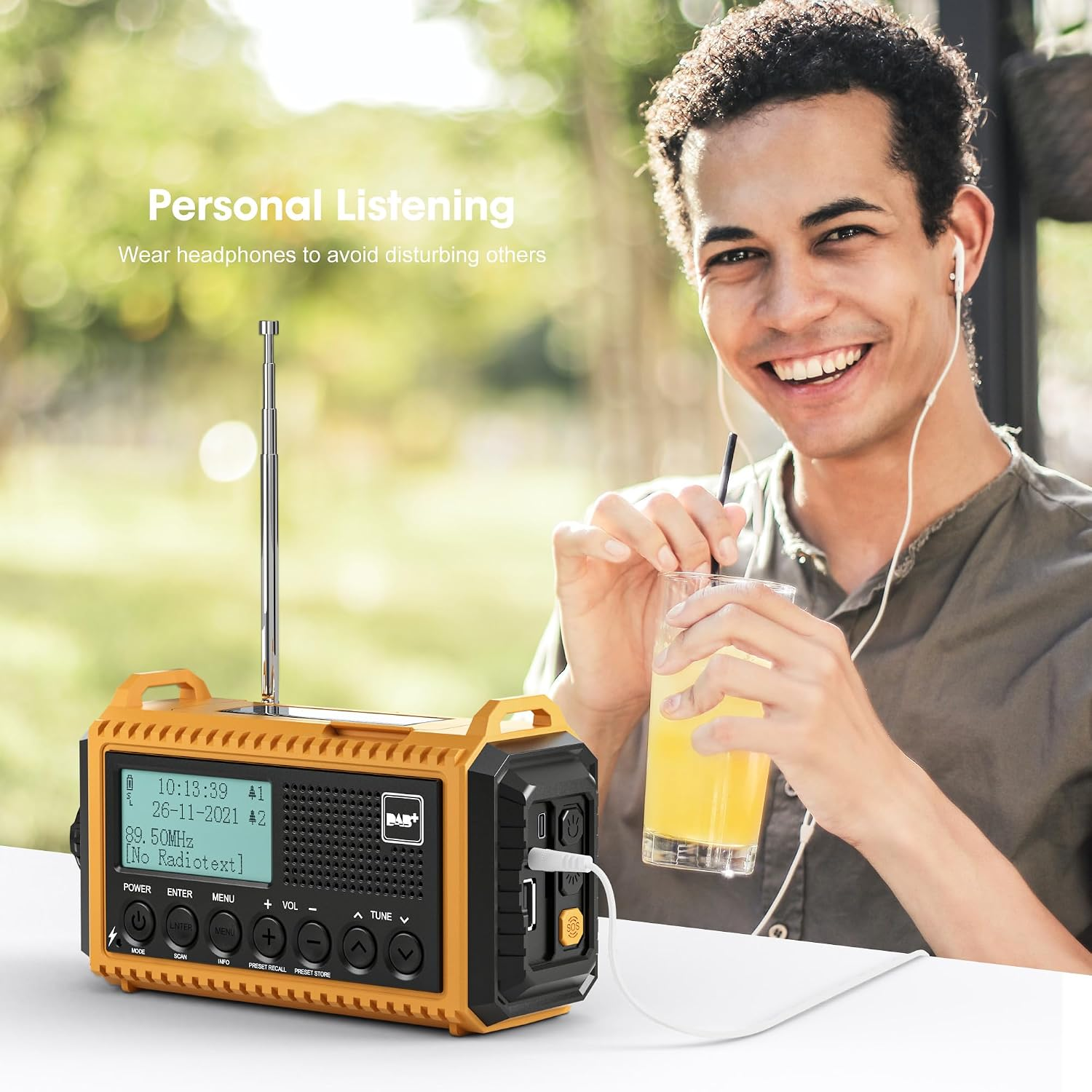 Ein lächelnder Mann mit Kopfhörern trinkt Orangensaft neben einem gelben Notfallradio auf einem Tisch.