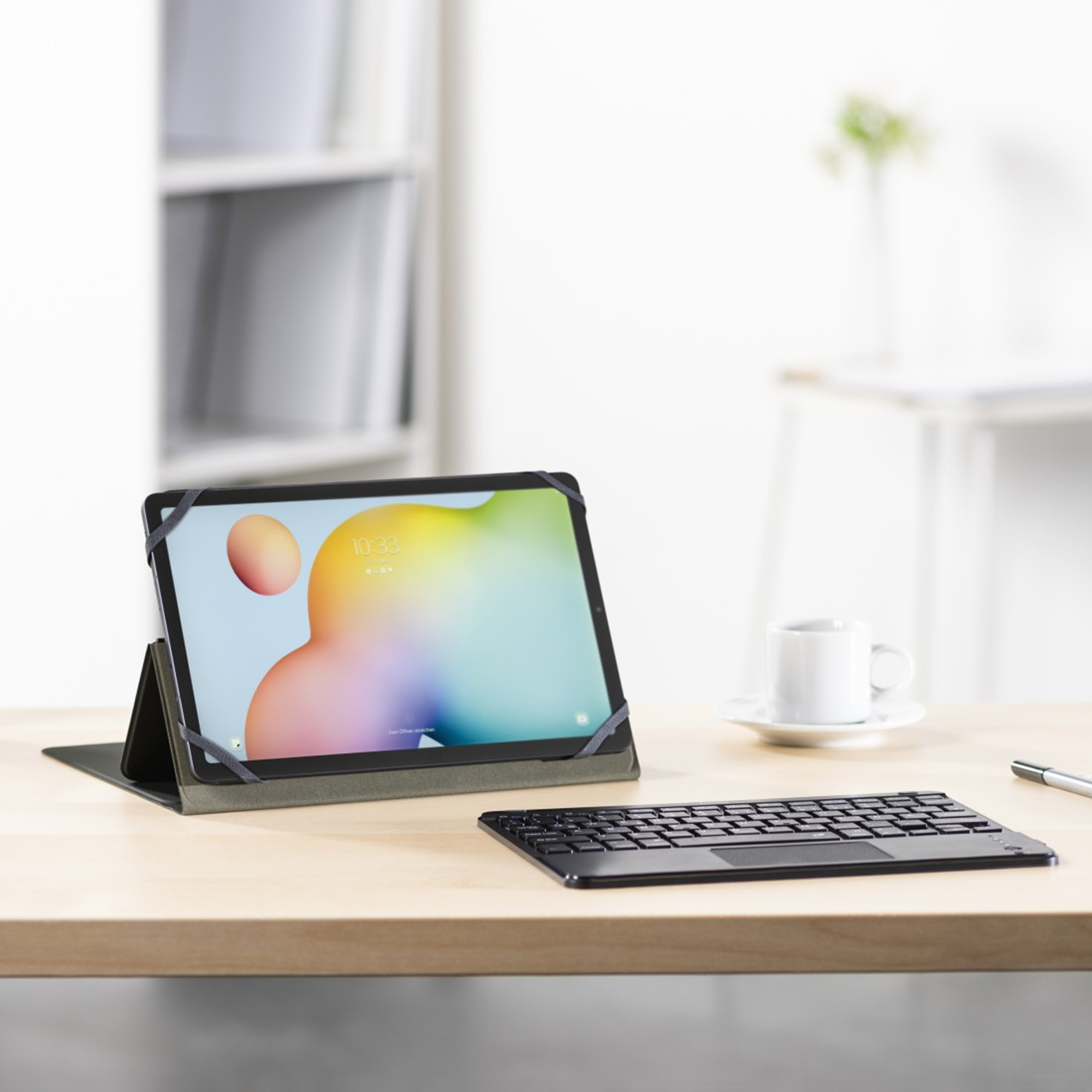 Un tablet in custodia con tastiera su scrivania in legno, con scaffale sfocato sullo sfondo.