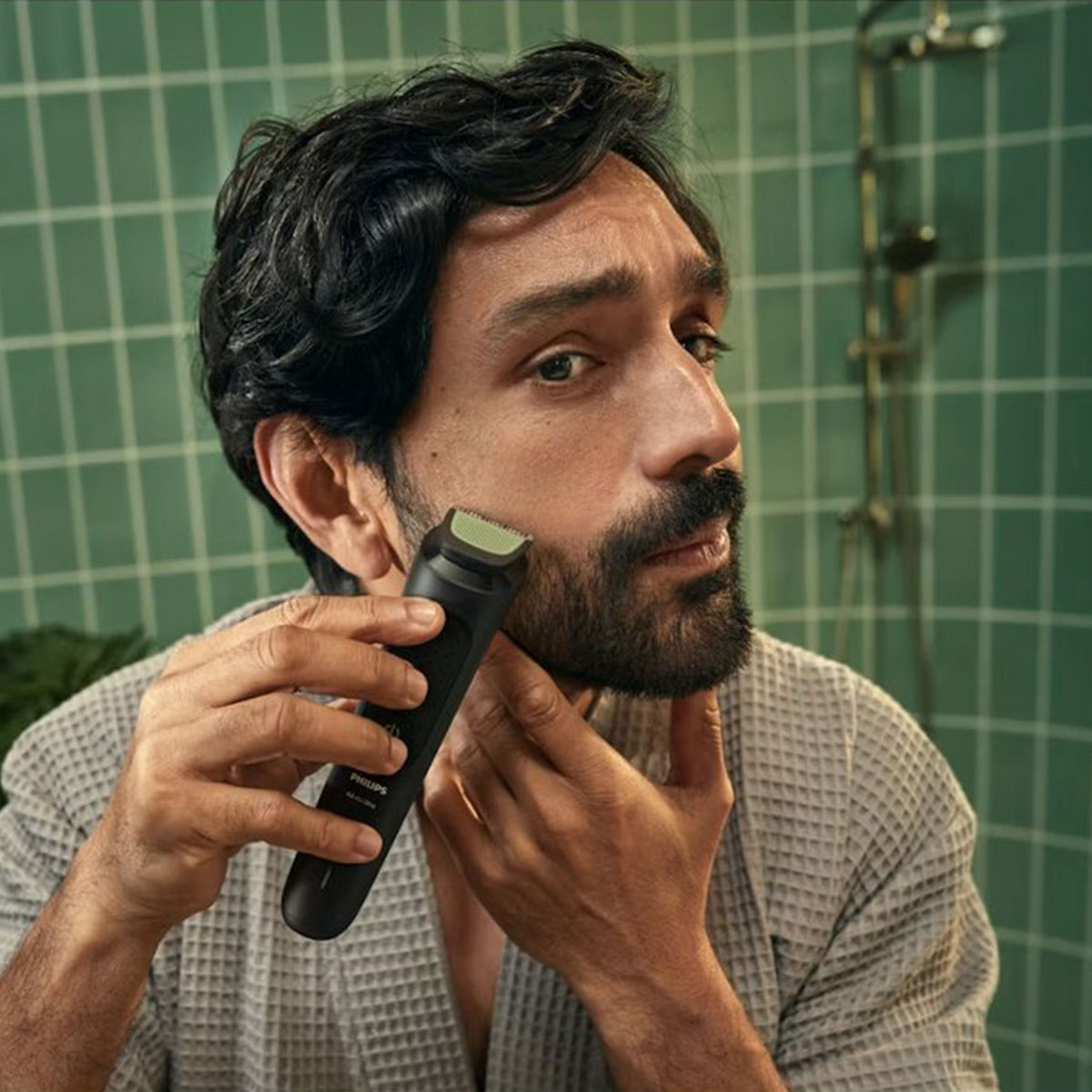 Sakallı bir adam banyoda siyah Philips tıraş makinesiyle sakalını kesiyor.