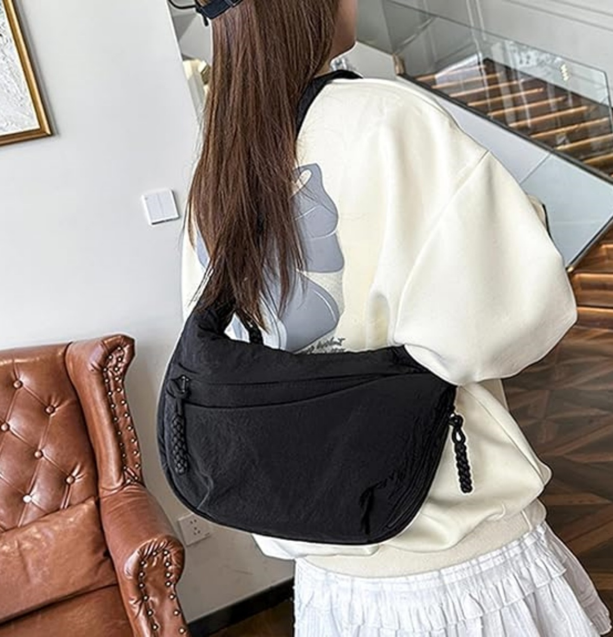 Eine Frau in weißem Pullover trägt eine schwarze Schultertasche.