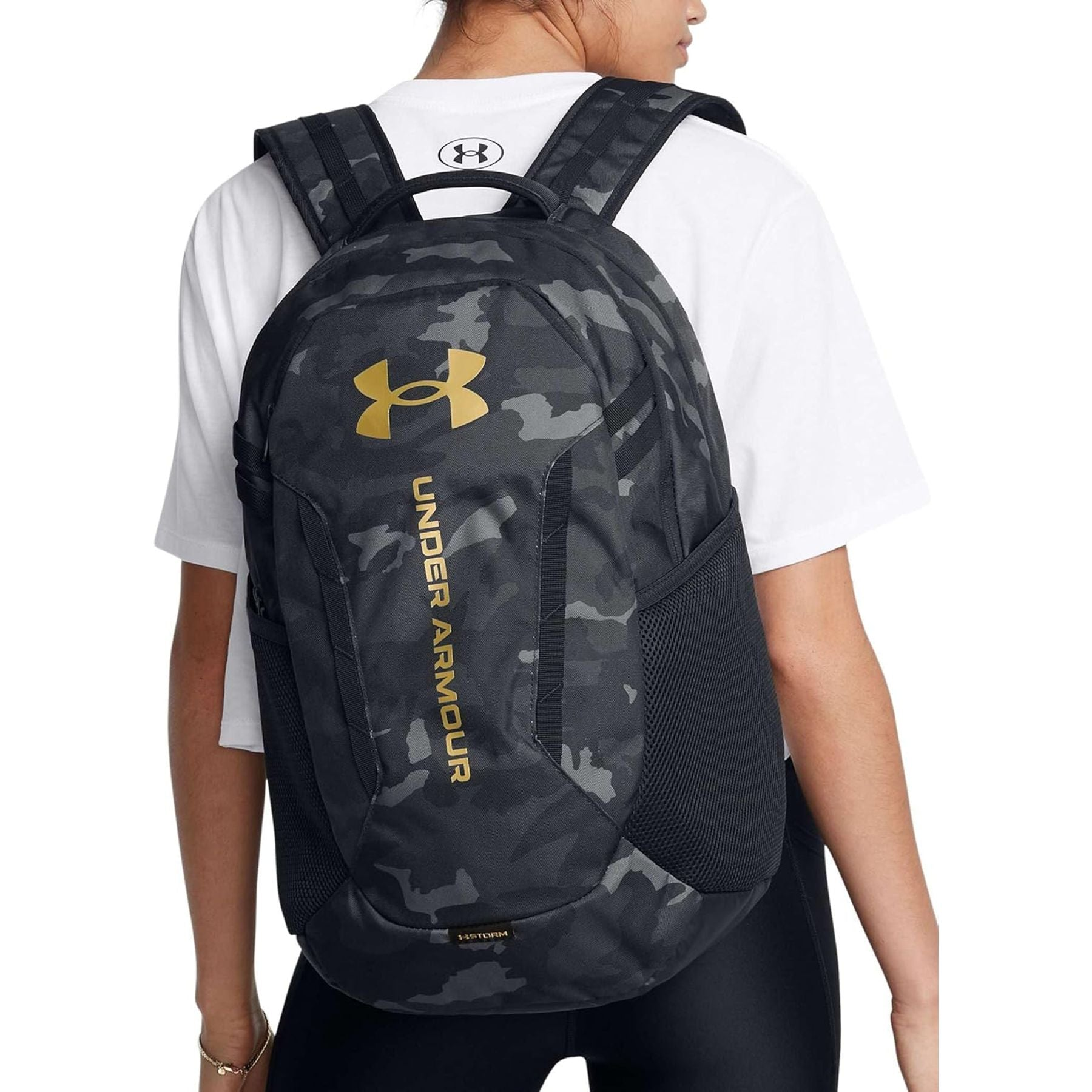 Eine Person trägt einen schwarz-grauen Tarnfarben-Rucksack von Under Armour.