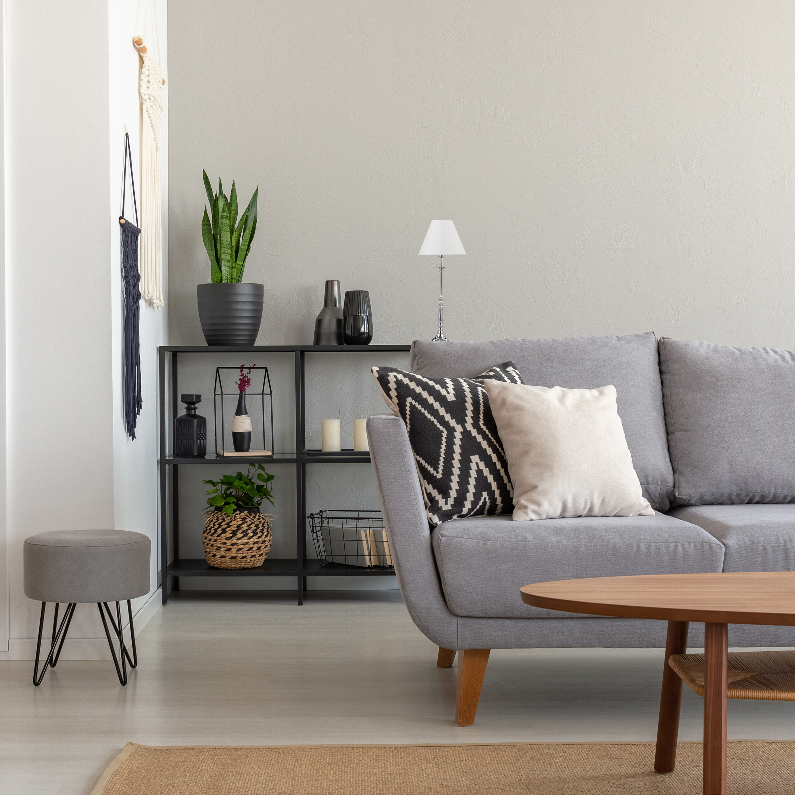 Gemütliches Wohnzimmer mit grauem Sofa, Kissen, schwarzem Regal mit Pflanzen und Deko, und Holztisch.