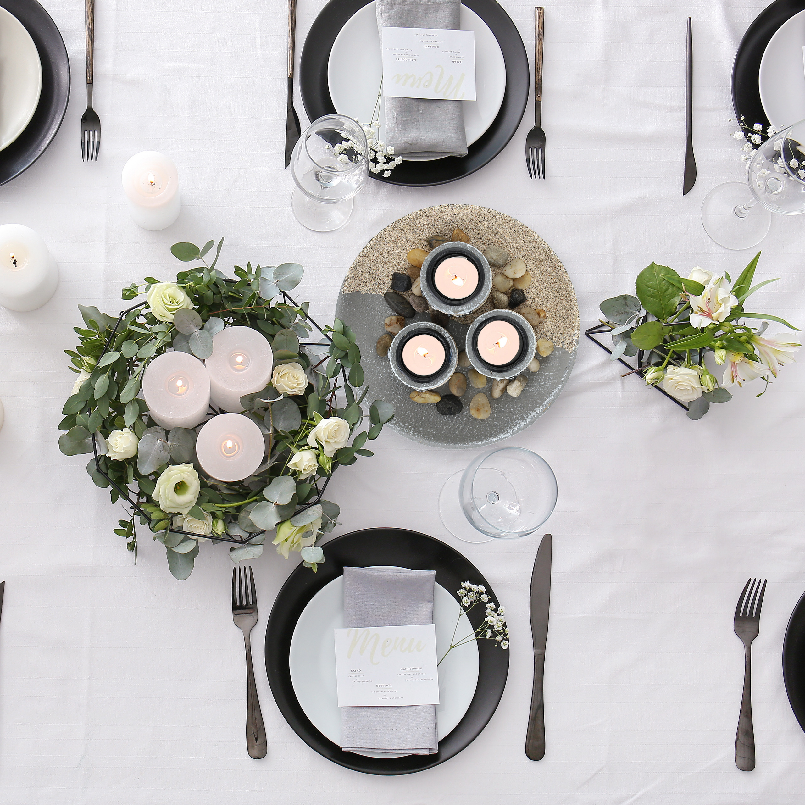 Festlich gedeckter Tisch mit Tellern, Servietten, Menükarten, Kerzen, Blumen und Besteck auf weißer Tischdecke.