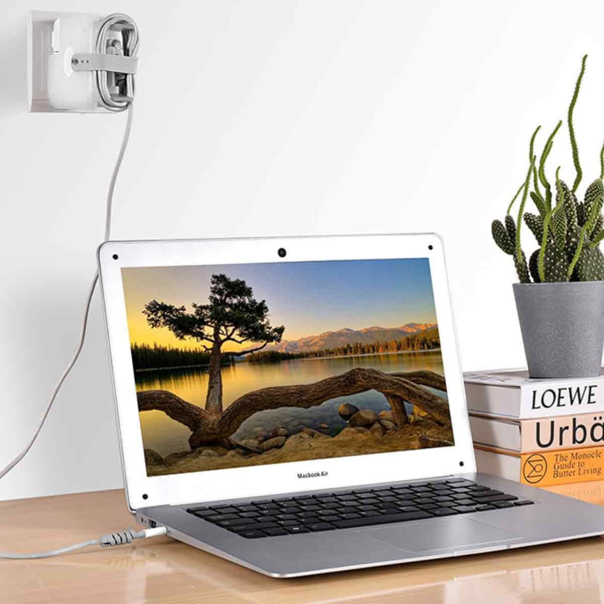 Ein Laptop steht auf einem Tisch, verbunden mit einem Wandladegerät. Rechts stehen Bücher und eine Topfpflanze.
