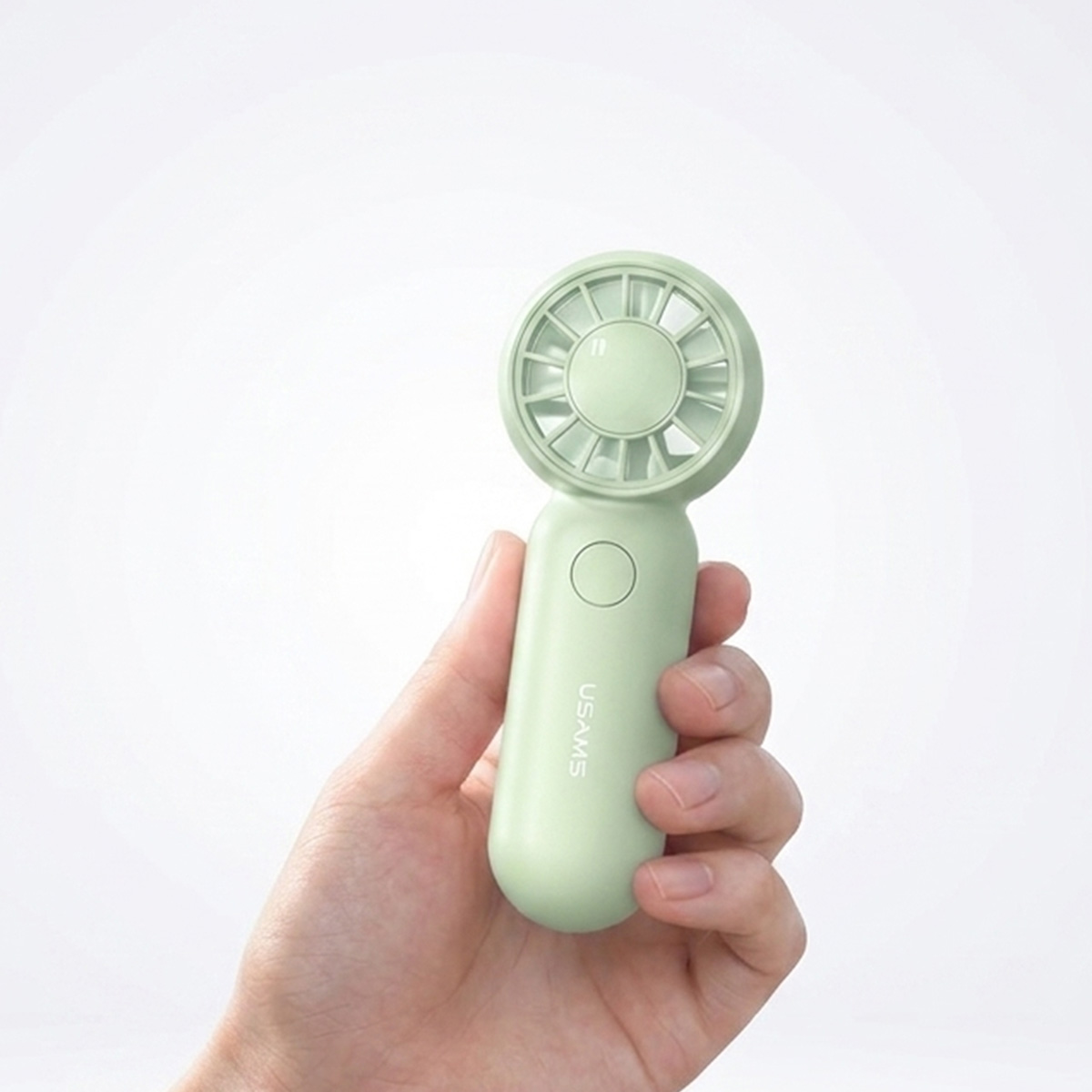 Eine Hand hält einen kleinen, hellgrünen Handventilator vor einem weißen Hintergrund.