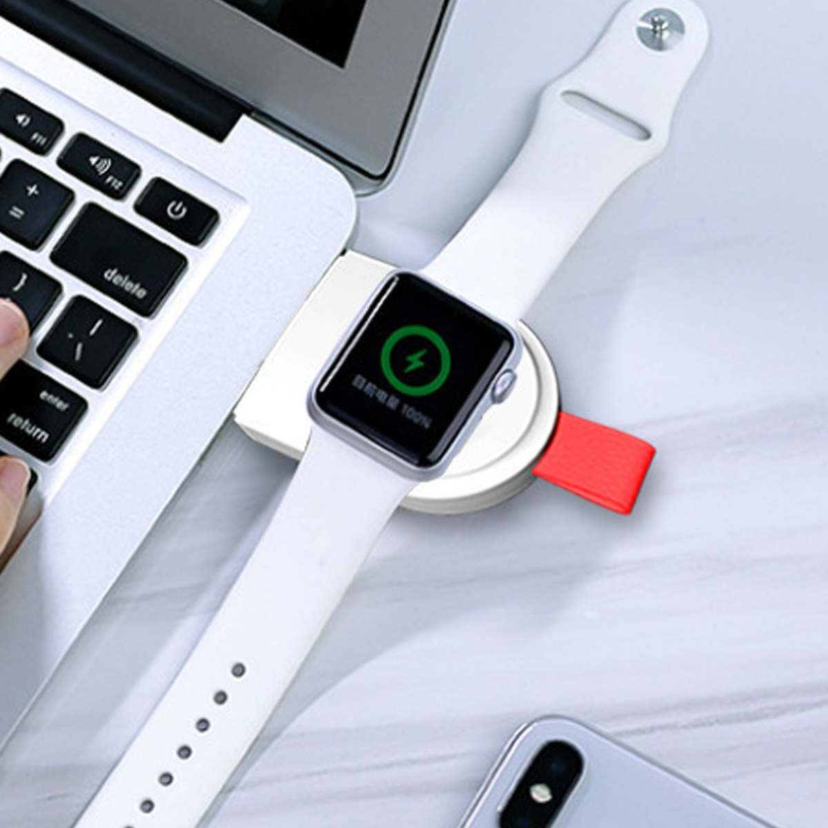 Eine weiße Smartwatch mit Lade-Dock liegt neben einer Laptop-Tastatur auf einem Tisch.
