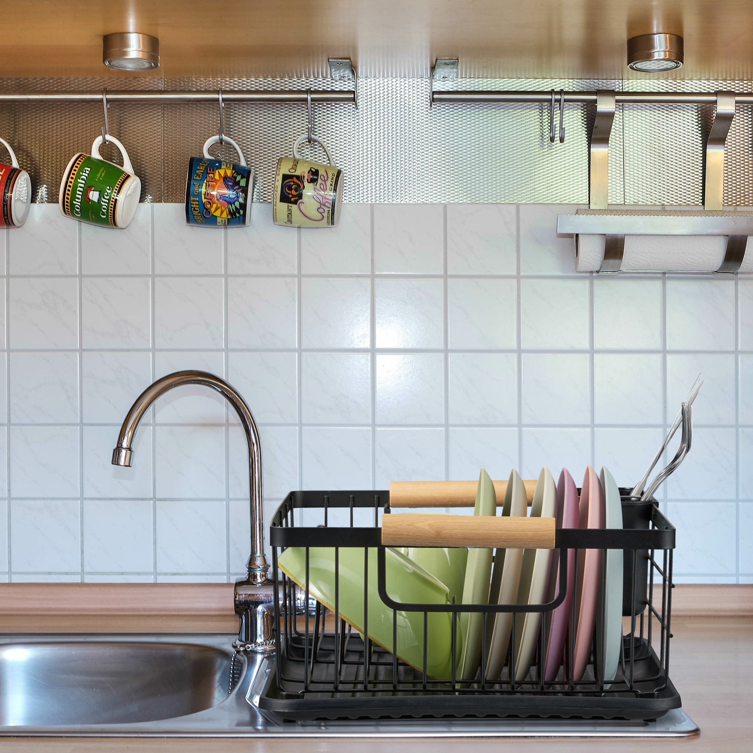 Ein Küchenwaschbecken mit Geschirrkorb, Chromarmatur und bunten Tassen darüber.