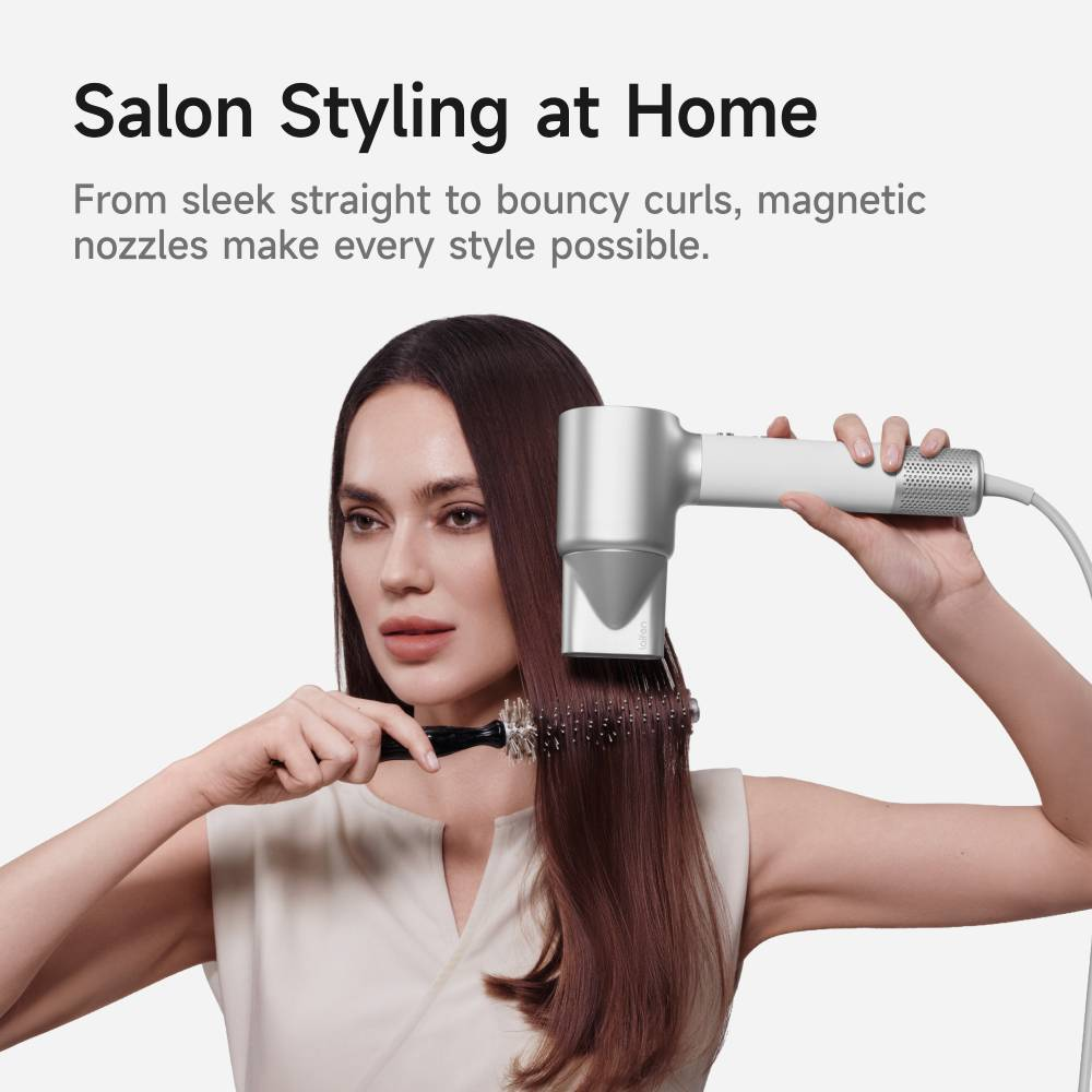 Una donna modella i suoi capelli lunghi e lisci usando un phon moderno e una spazzola rotonda.
