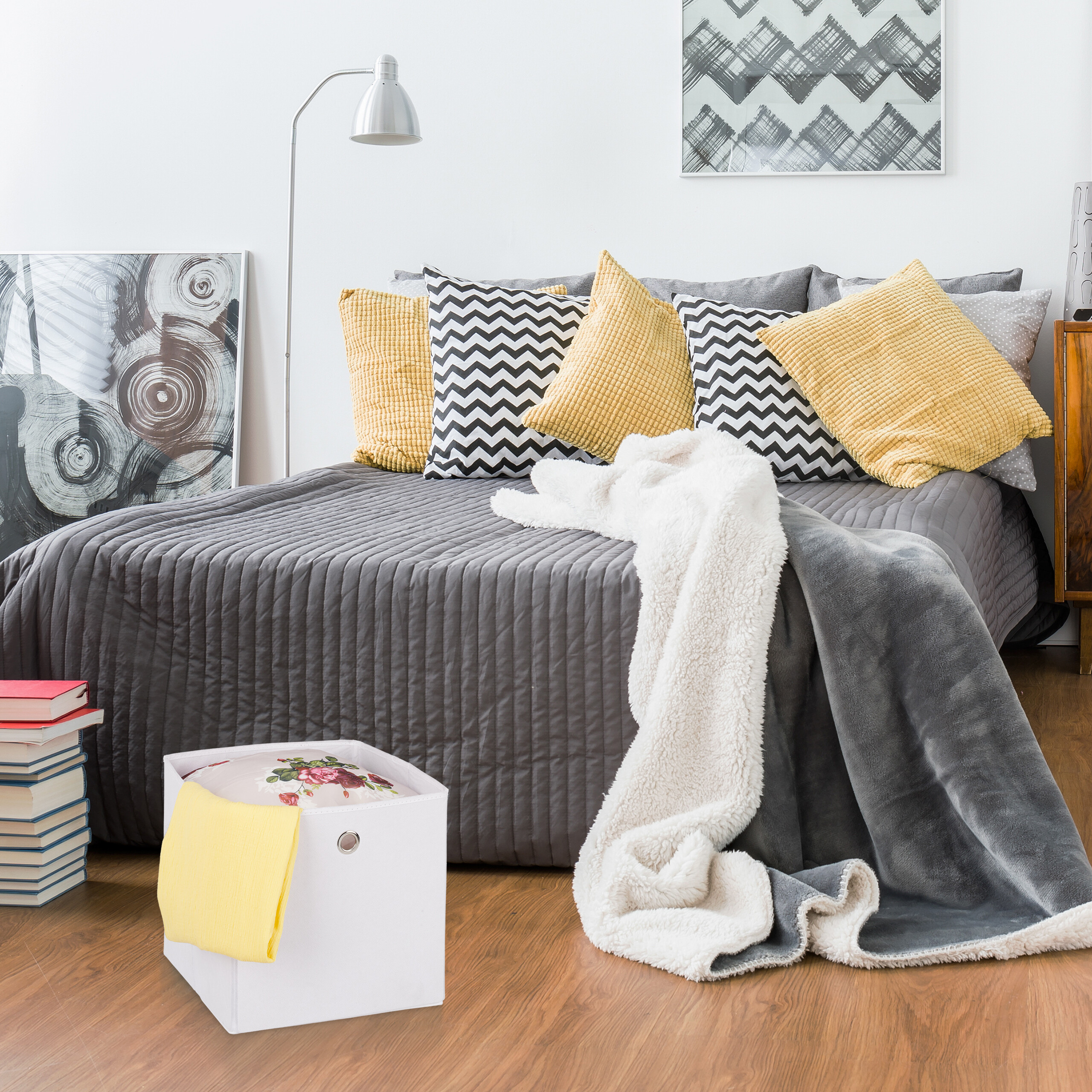 Ein Bett mit grauer Bettwäsche, gelben und Zickzack-Kissen, einer weißen Decke und einer weißen Aufbewahrungsbox.