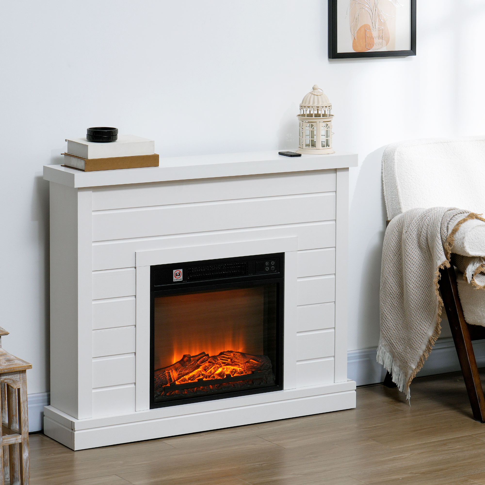 Una chimenea eléctrica blanca contra una pared con libros apilados, un farol y un sillón al lado.
