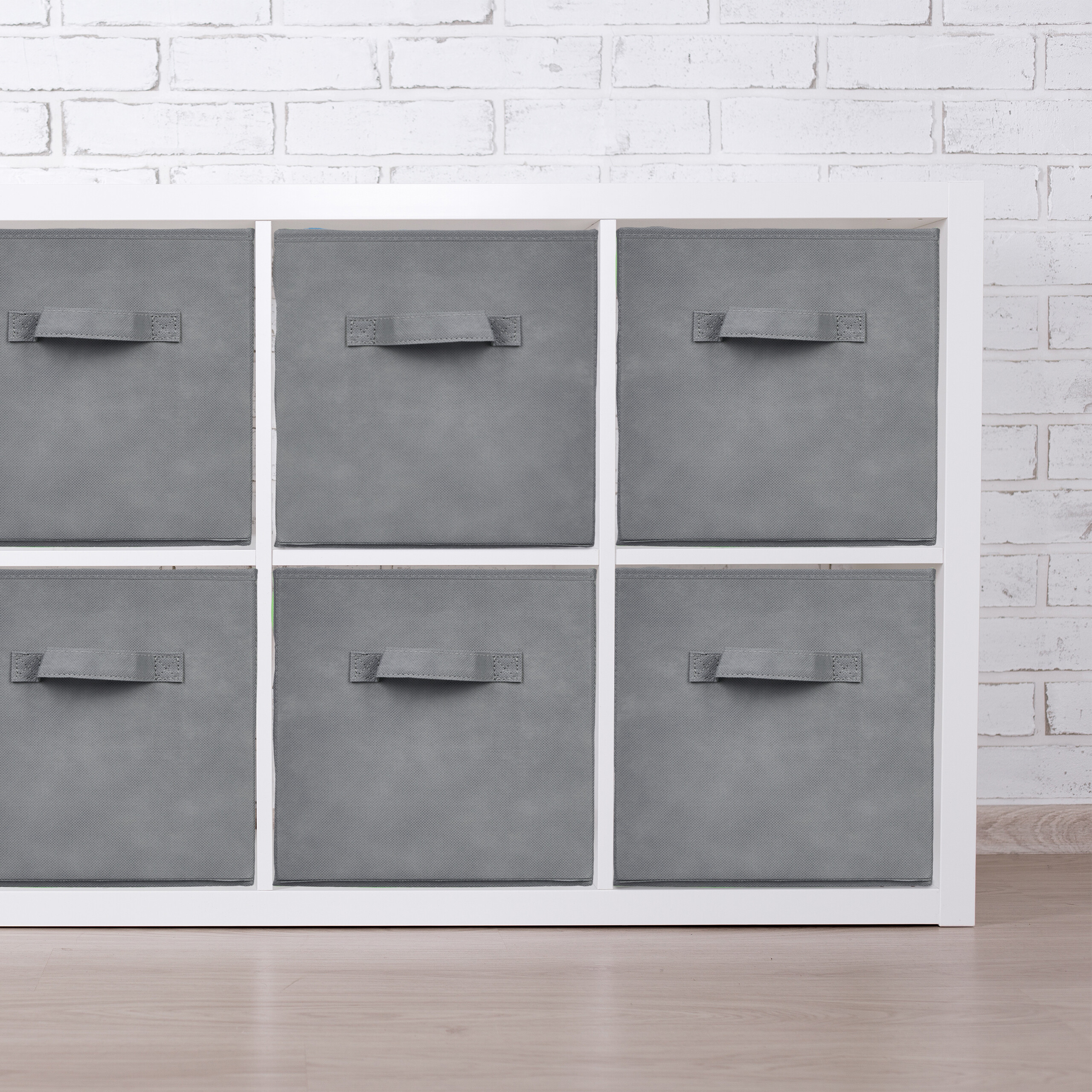 Ein weißes Regal mit sechs grauen Stoffboxen vor einer weißen Backsteinwand.