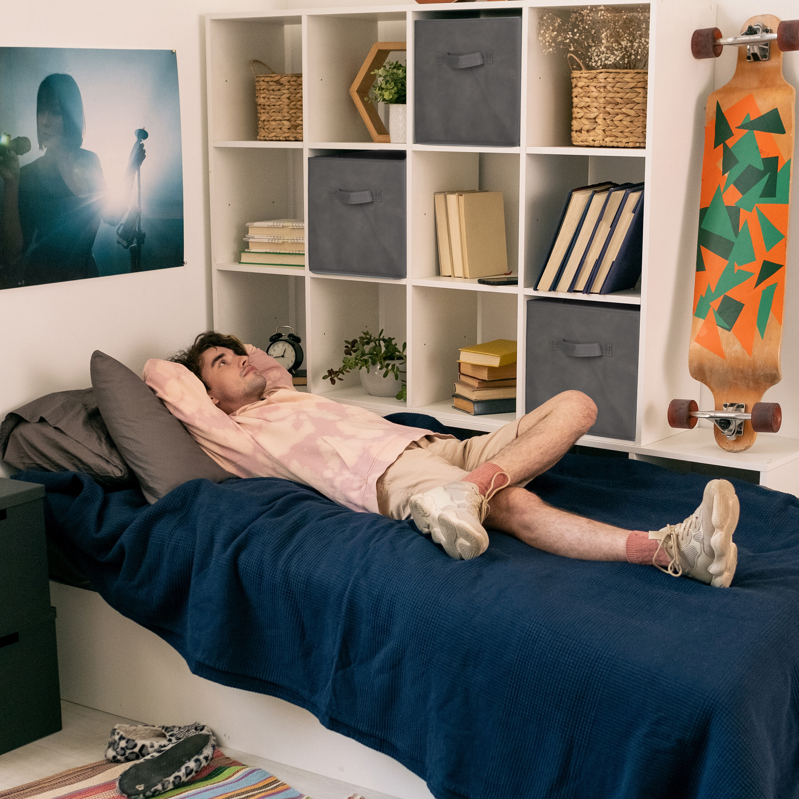 Ein junger Mann liegt entspannt auf einem blauen Bett in seinem Zimmer vor einem weißen Regal.