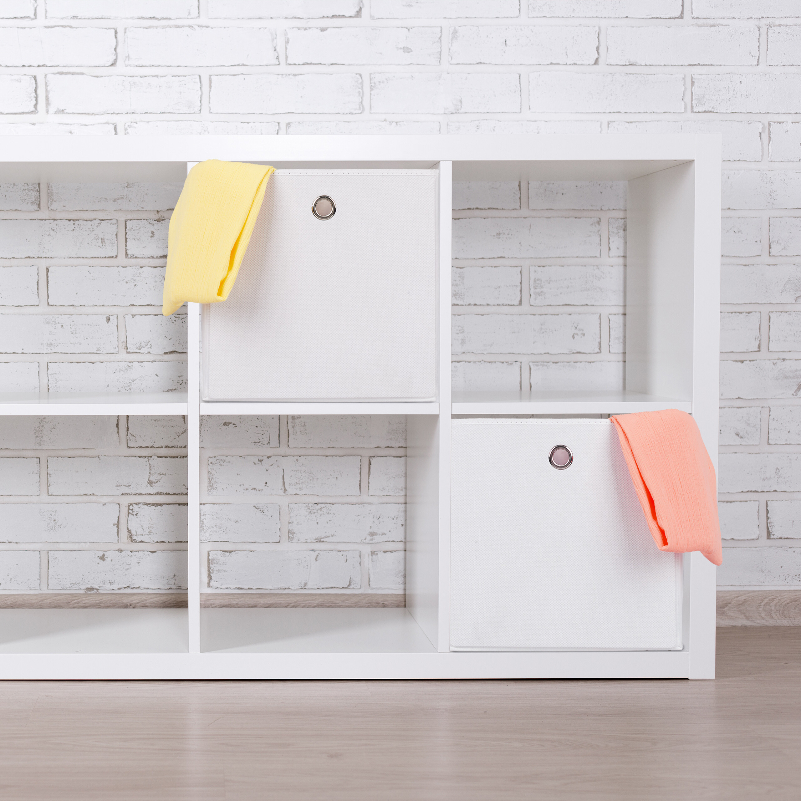 Weißes Regal mit bunten Stoffboxen und Handtüchern vor einer Ziegelwand.