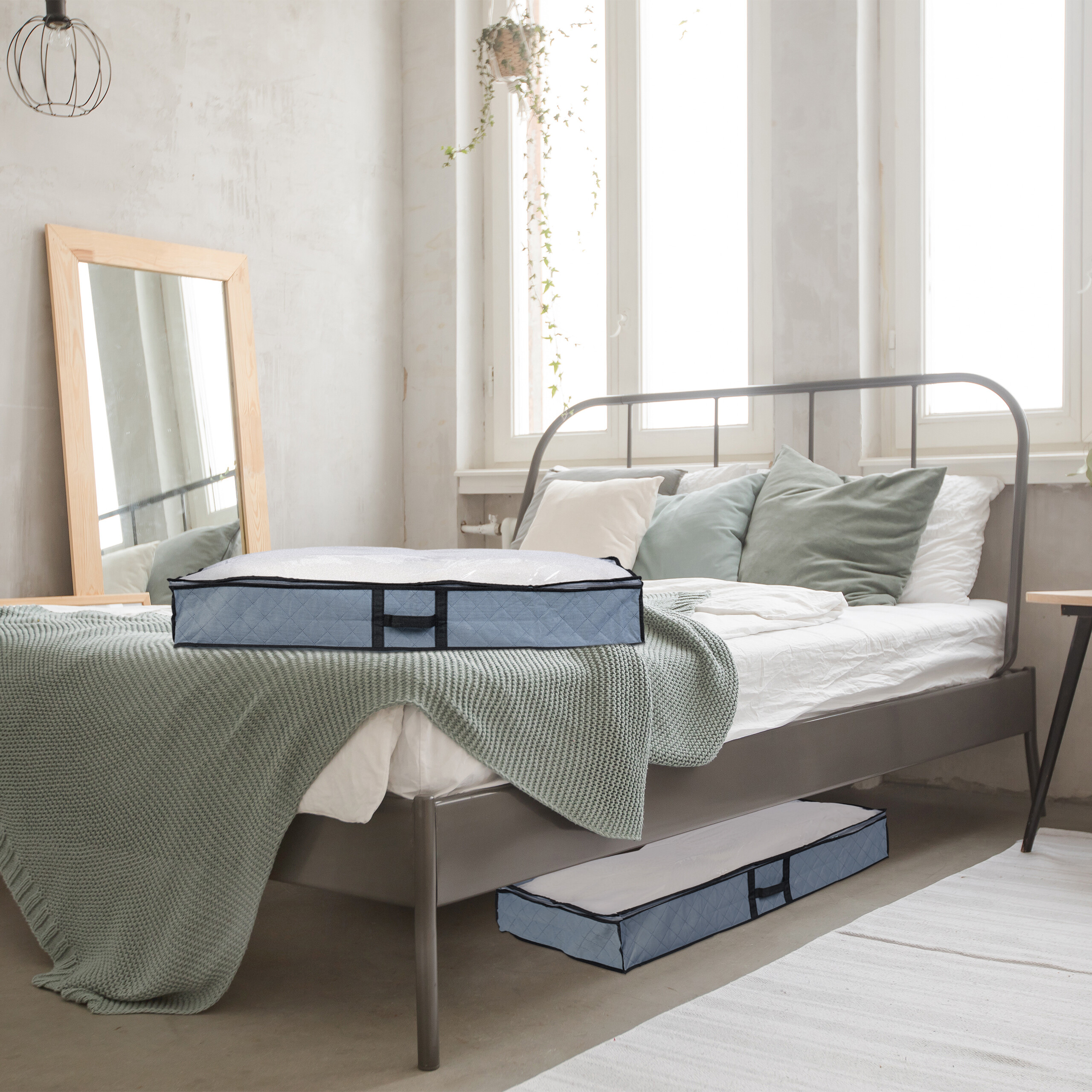Zwei blaue Aufbewahrungstaschen auf und unter einem Bett im hellen Schlafzimmer mit großen Fenstern und Spiegel.