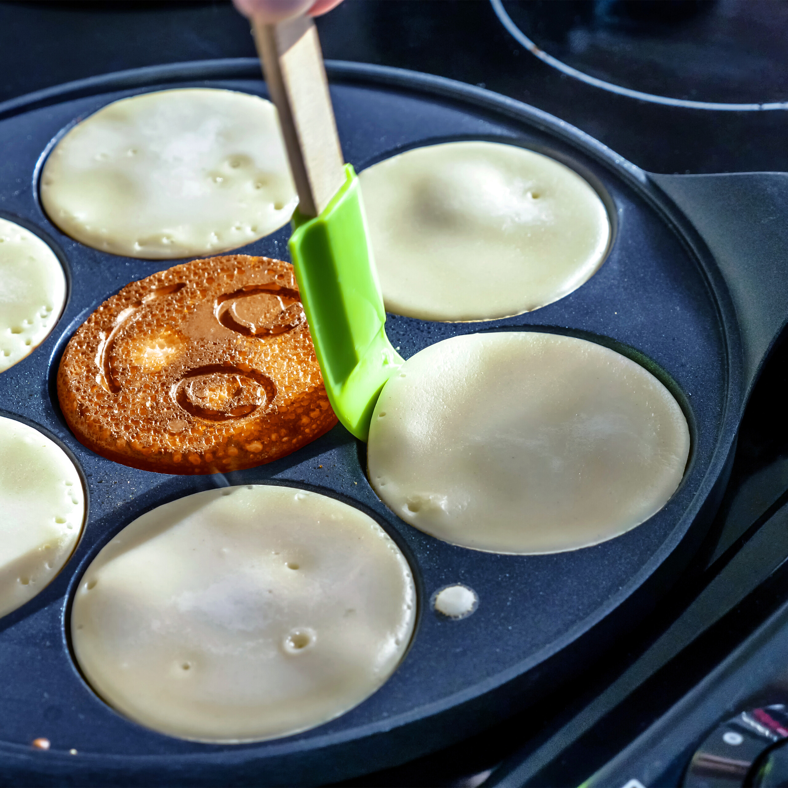 Pfannkuchen braten in einer speziellen Pfanne, einer hat ein Smiley-Gesicht.