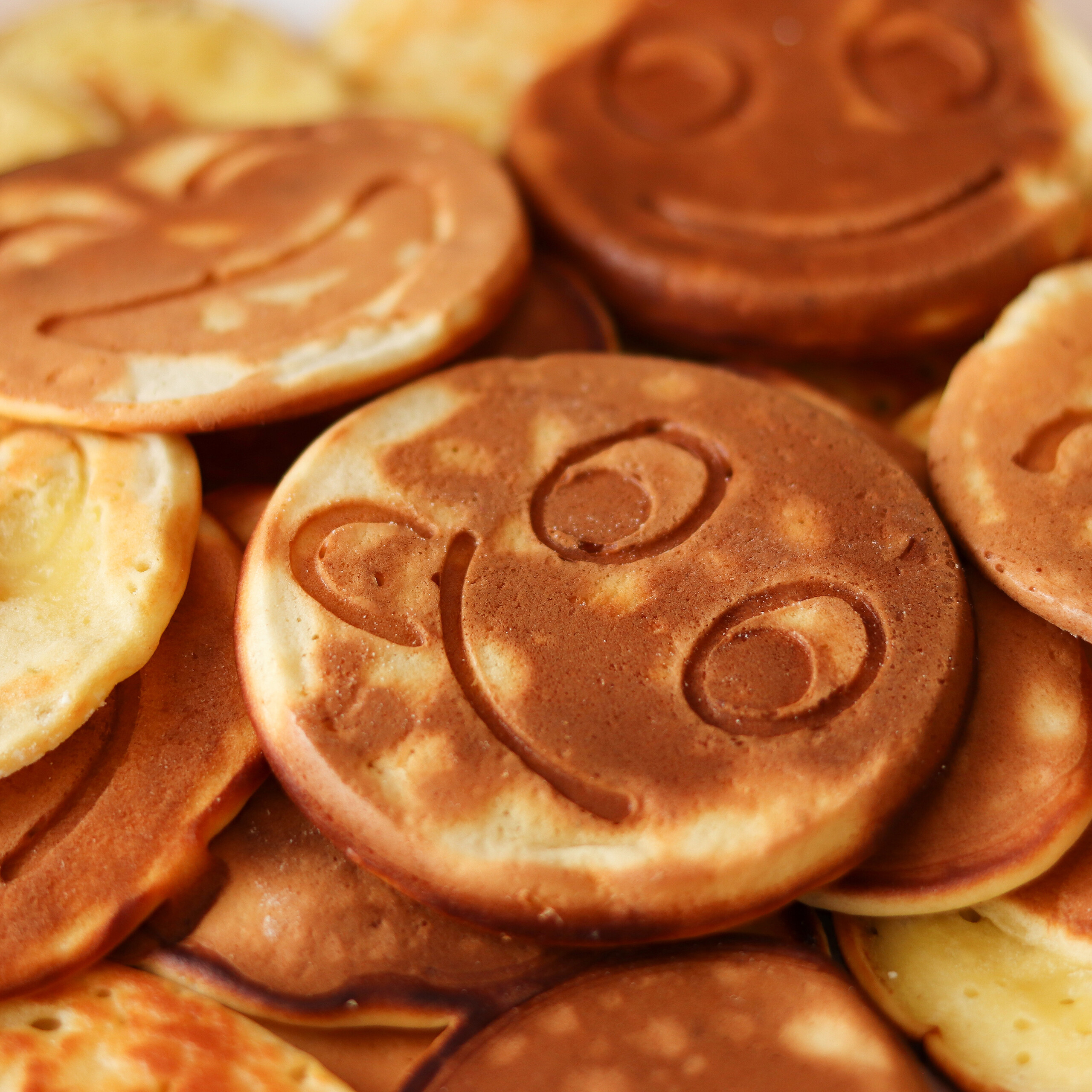 Ein Stapel kleiner goldbrauner Pfannkuchen mit eingeprägten lächelnden Gesichtern.