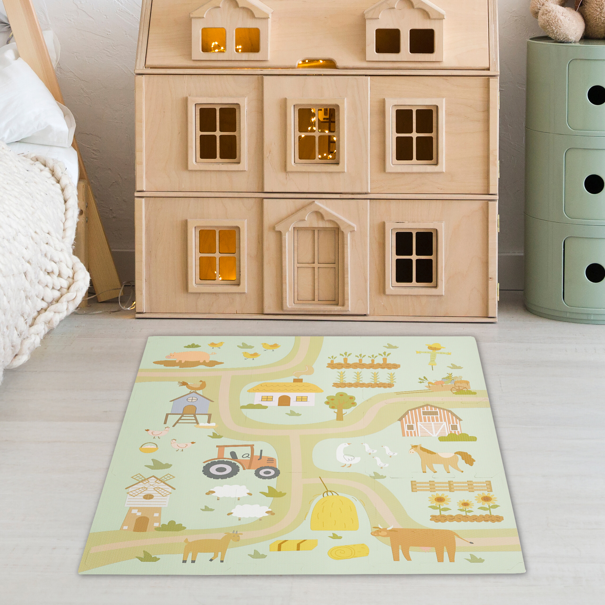 Ein großes Holzpuppenhaus steht auf dem Boden neben einem grünem Schrank und einem Spielteppich mit Bauernhofmotiv.