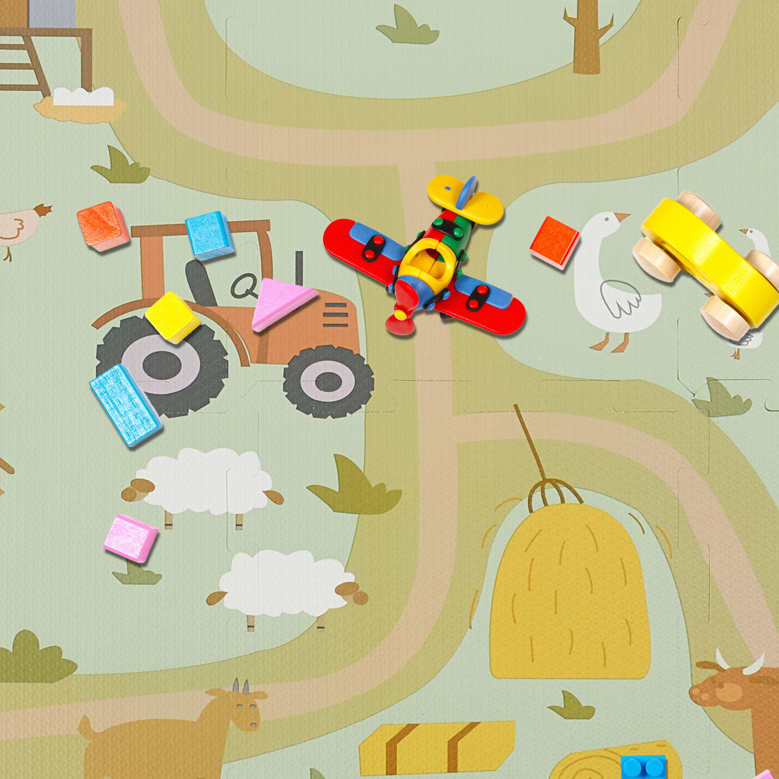 Buntes Kinderspielzeug liegt auf einer Spielmatte mit Bauernhofmotiv.