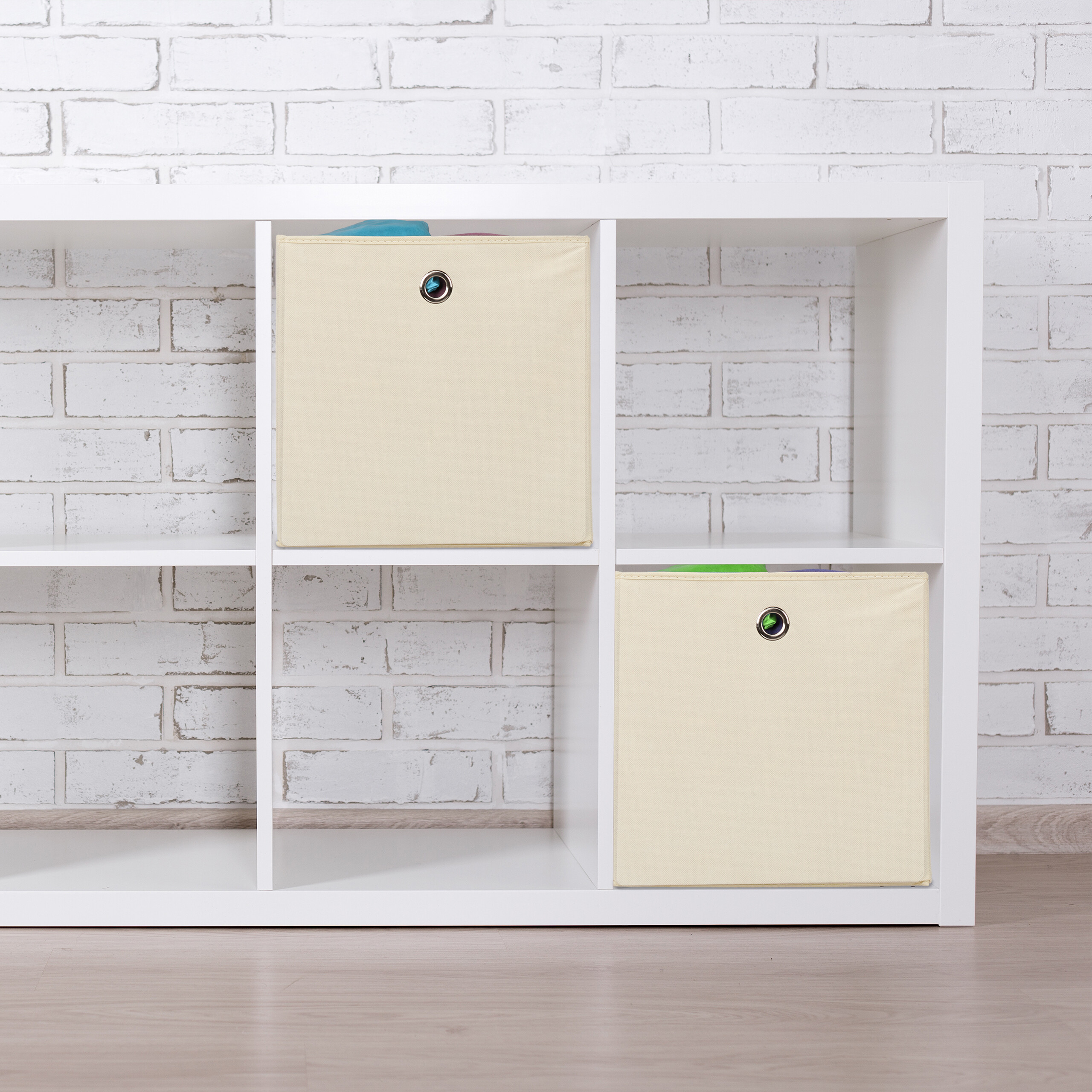 Ein weißes Regalsystem mit beigen Aufbewahrungsboxen vor einer weißen Backsteinwand.