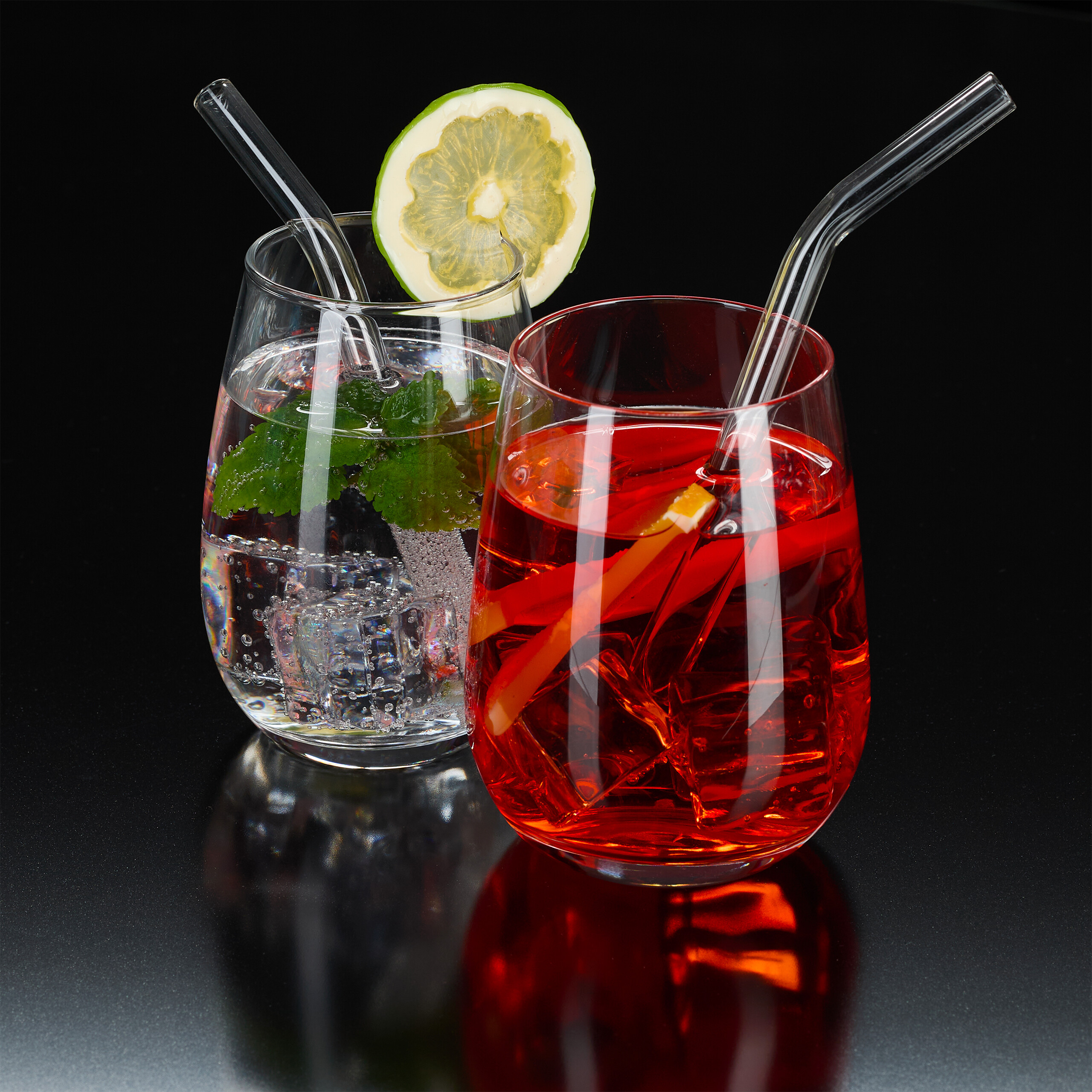 Zwei Gläser Cocktails mit Eis und Strohhalmen auf dunklem Hintergrund. Eines ist klar, das andere ist rot.