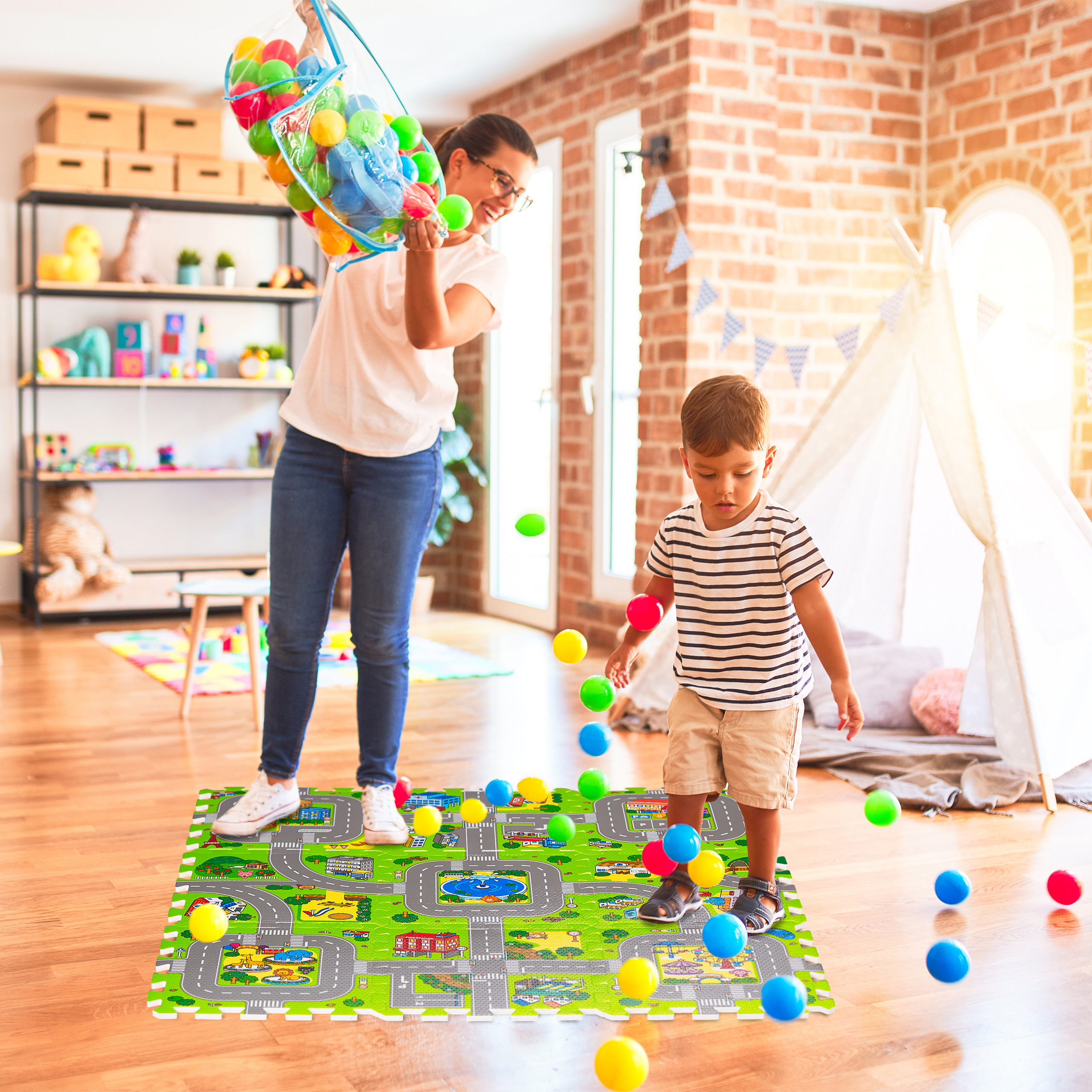Eine Frau schüttet bunte Bälle aus einer Tasche auf eine Spielmatte, während ein Junge daneben steht.
